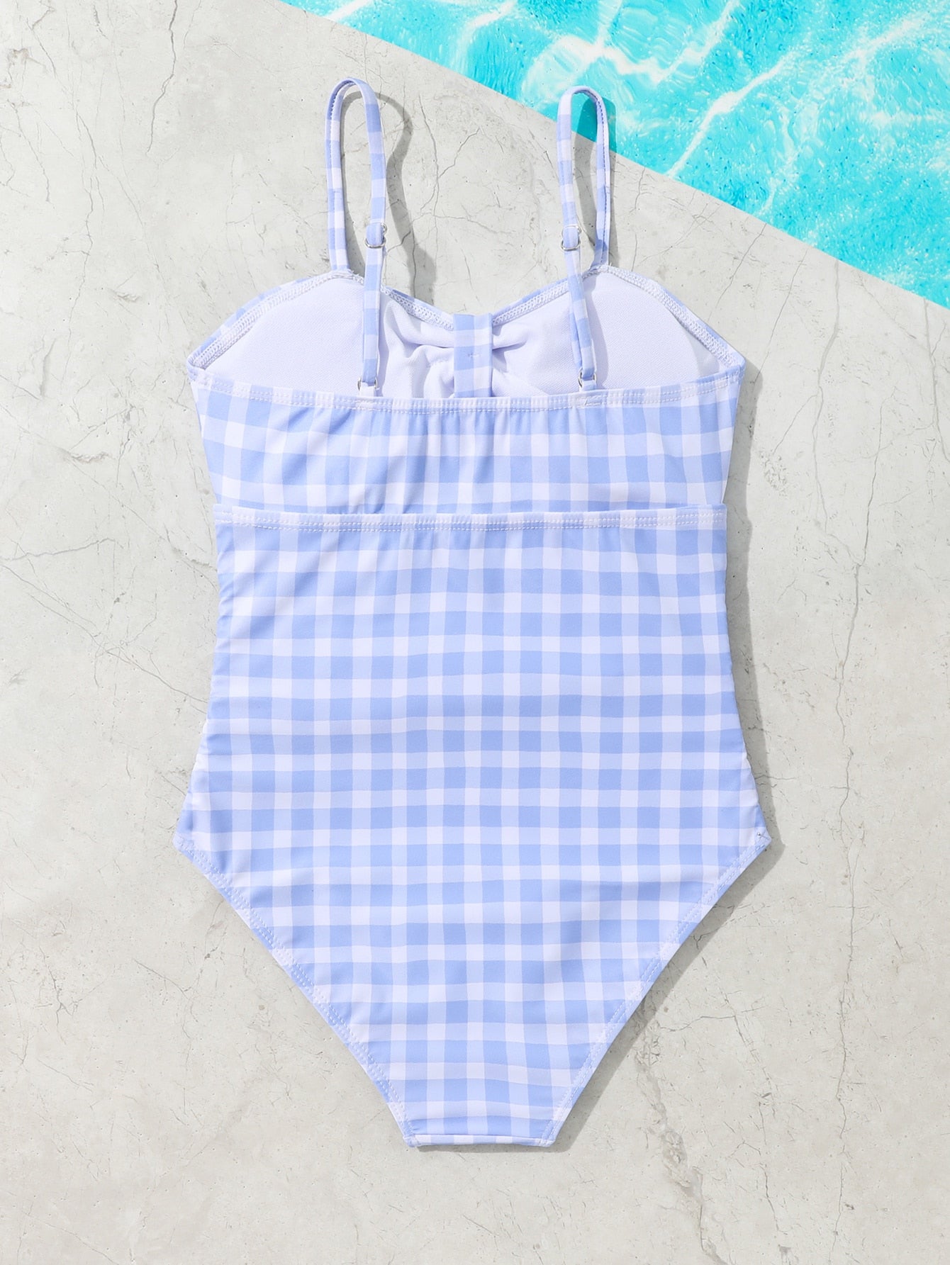 Blue and white gingham one-piece swimsuit for tween girls with cut-out detail, knot front, spaghetti straps, and lined high-stretch fabric.