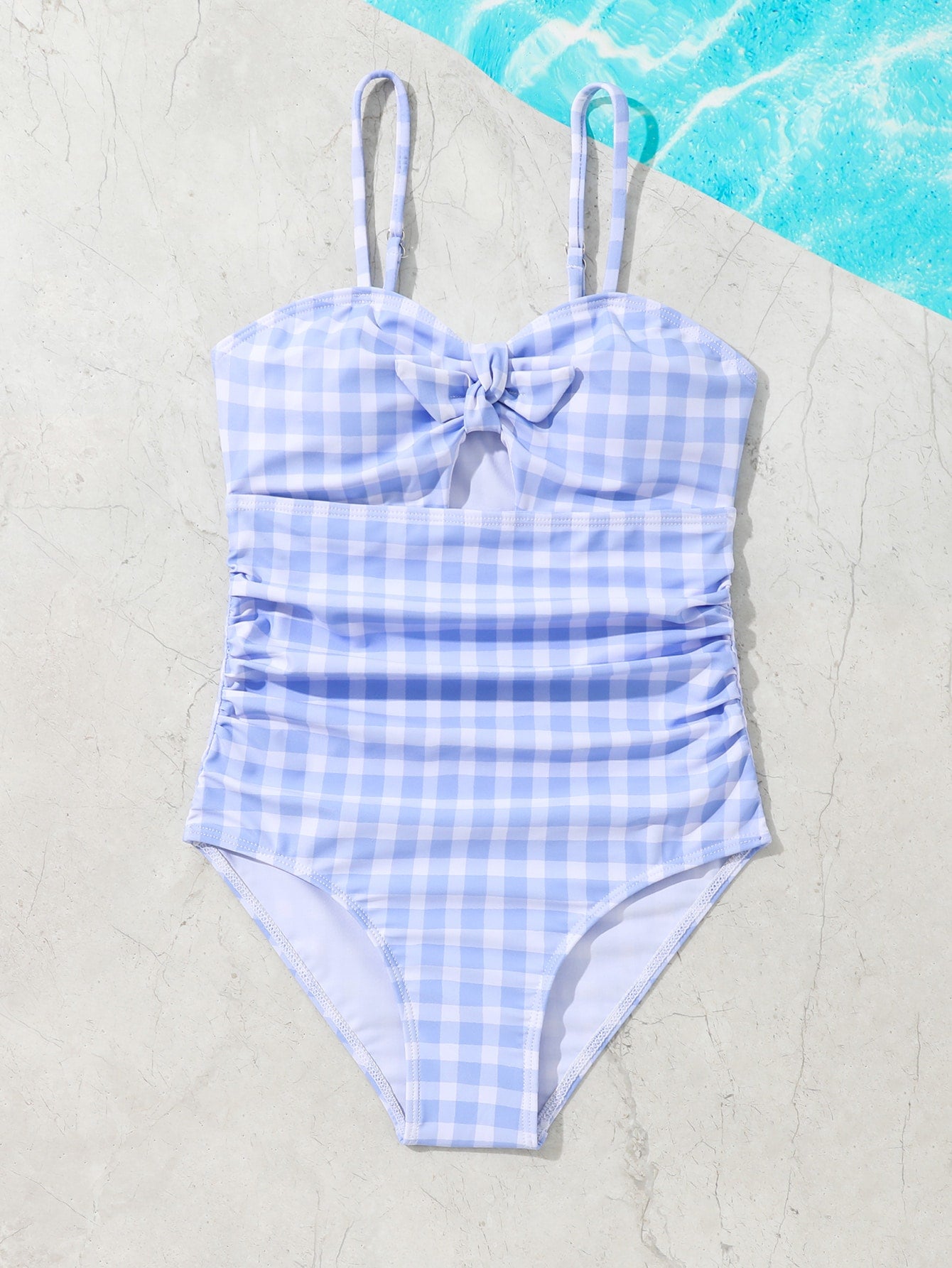 Blue and white gingham one-piece swimsuit for tween girls with cut-out detail, knot front, spaghetti straps, and lined high-stretch fabric.