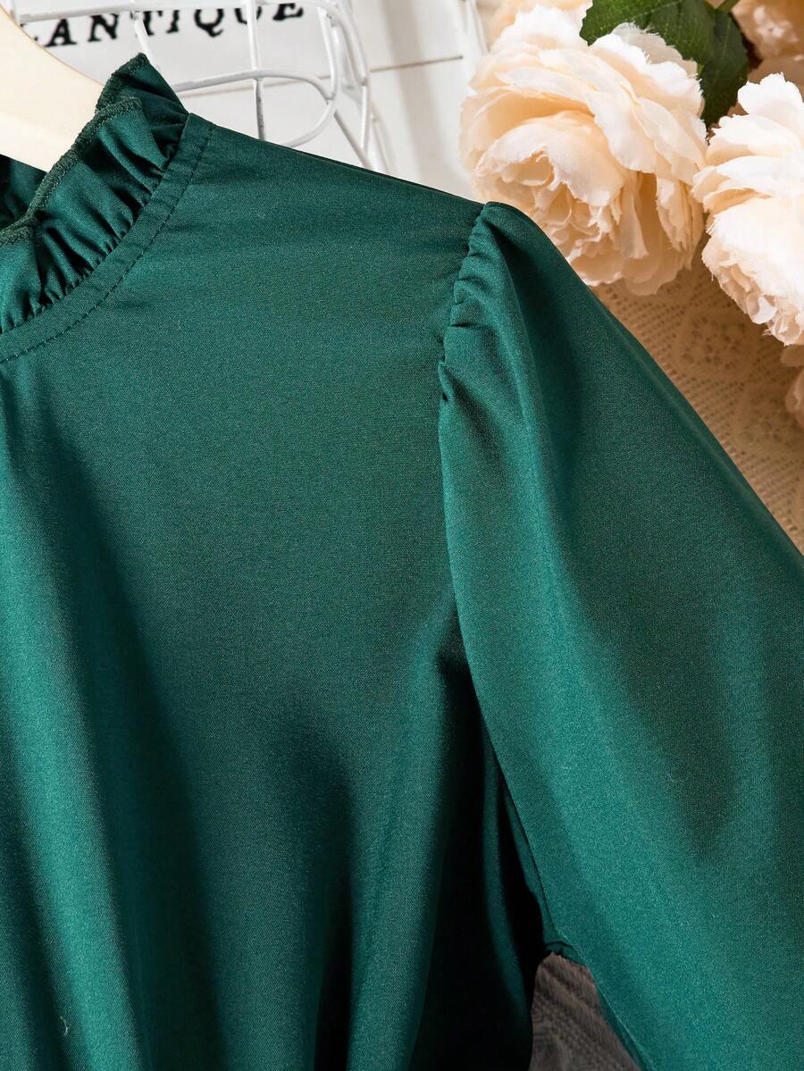 Tween girl wearing a royal blue long sleeve pleated casual A-line dress featuring a stand collar, flare sleeves, high waist with front tie belt, and ruffle hem.