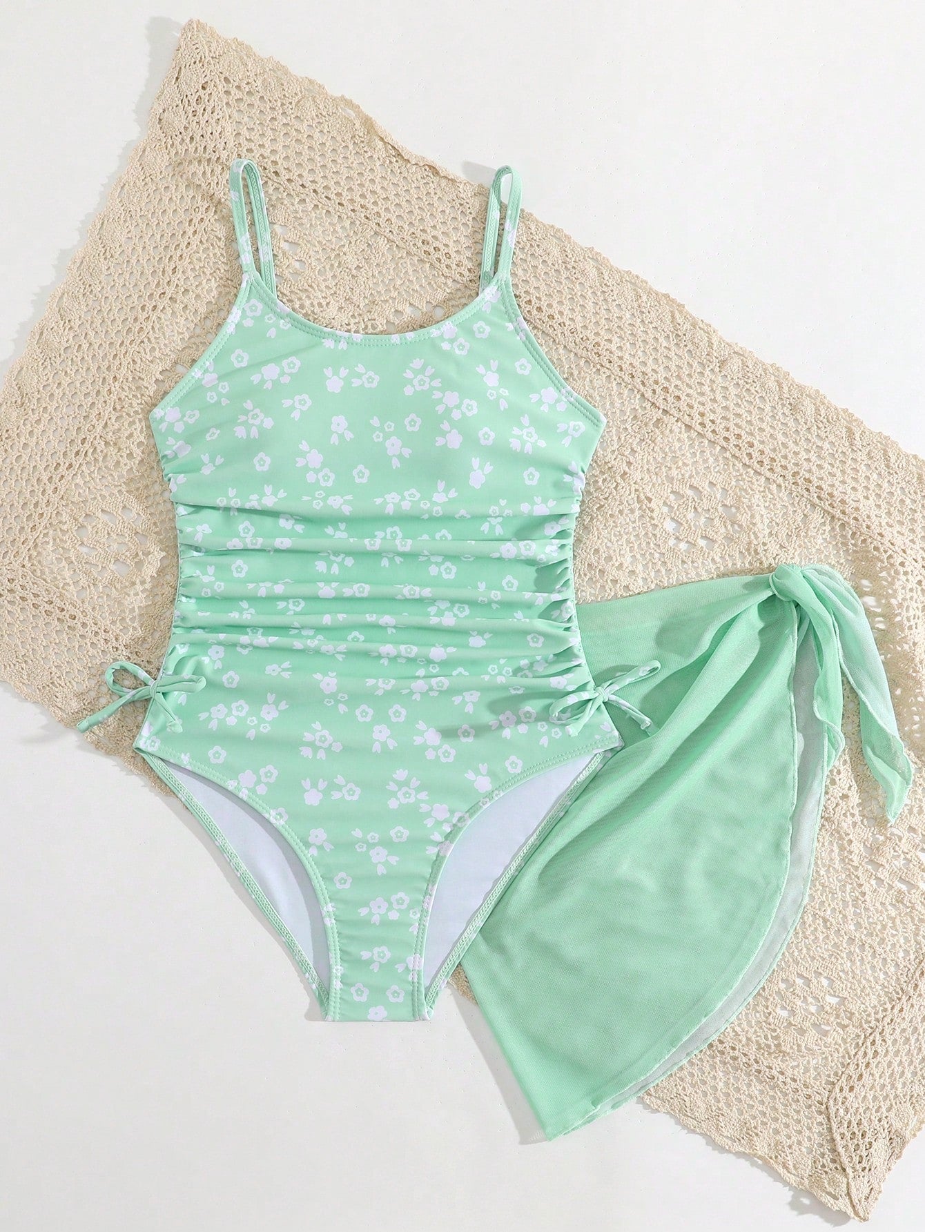Tween girls 2-piece swimsuit in black with pink floral print, featuring spaghetti straps, bow decor, mesh detail, and a skirted mid-waist bottom. Sleeveless vacation-style swim set with medium-stretch fabric.
