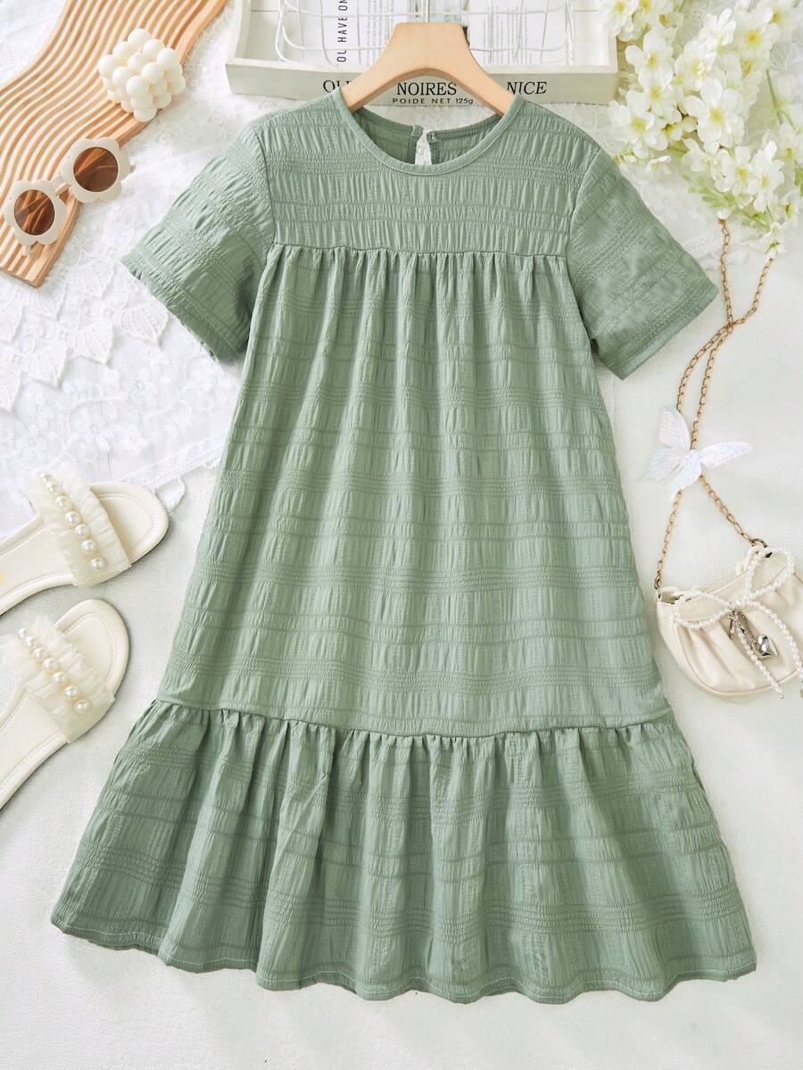Tween girl wearing an Army Green textured short sleeve smock midi dress with round neck and ruffle flounce hem.