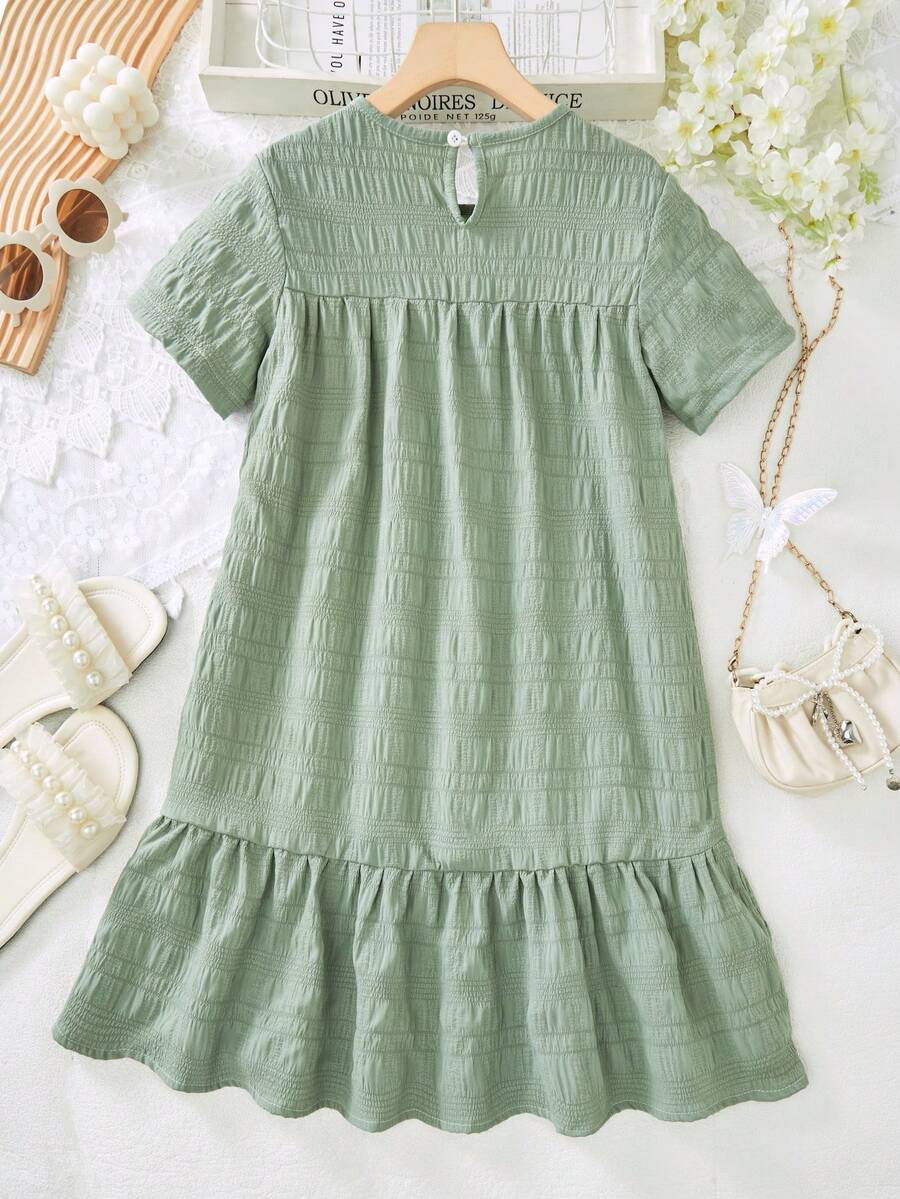 Tween girl wearing an Army Green textured short sleeve smock midi dress with round neck and ruffle flounce hem.