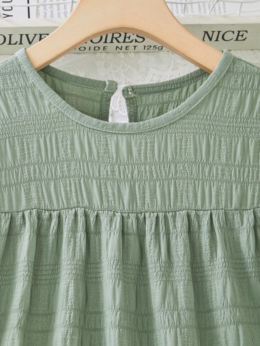Tween girl wearing an Army Green textured short sleeve smock midi dress with round neck and ruffle flounce hem.