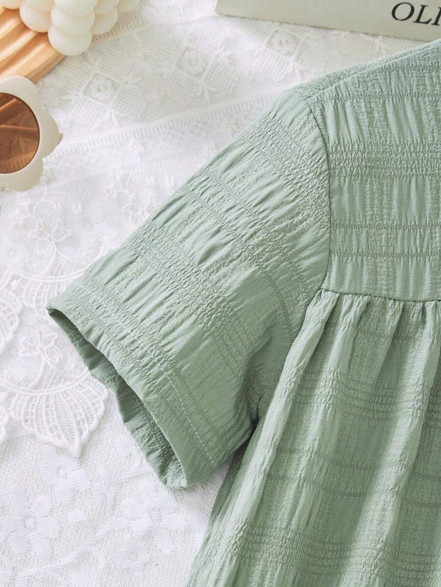 Tween girl wearing an Army Green textured short sleeve smock midi dress with round neck and ruffle flounce hem.