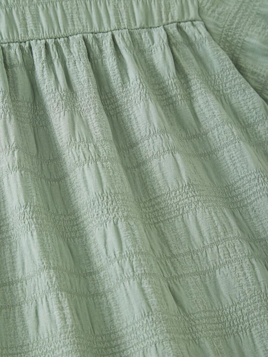 Tween girl wearing an Army Green textured short sleeve smock midi dress with round neck and ruffle flounce hem.