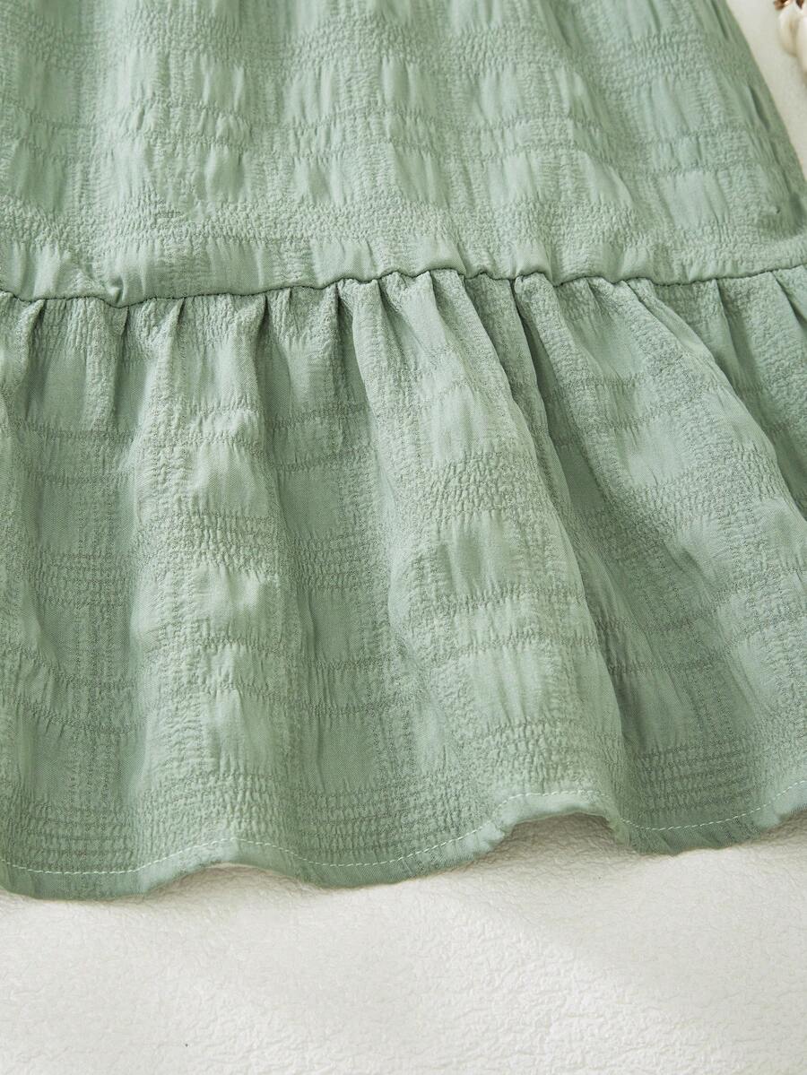 Tween girl wearing an Army Green textured short sleeve smock midi dress with round neck and ruffle flounce hem.