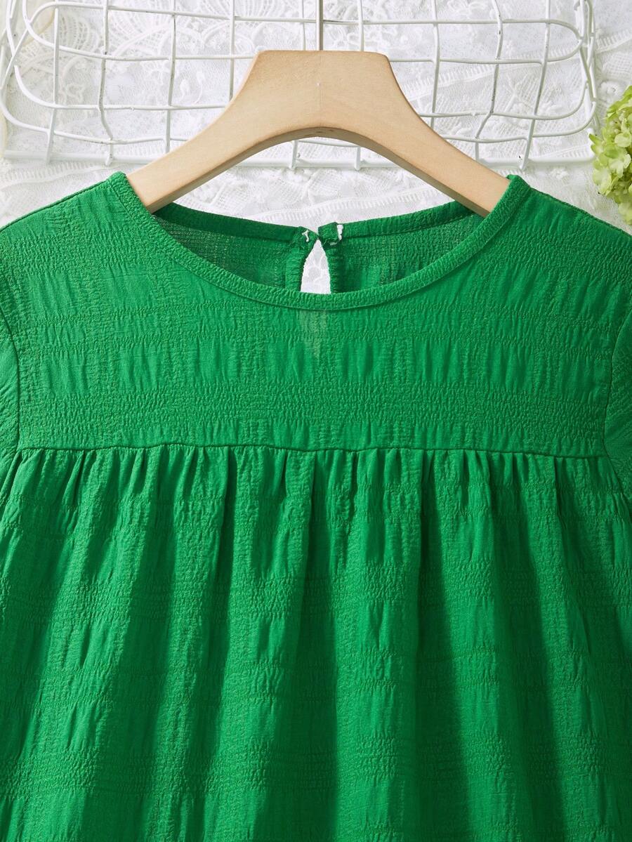 Tween girl wearing an Army Green textured short sleeve smock midi dress with round neck and ruffle flounce hem.