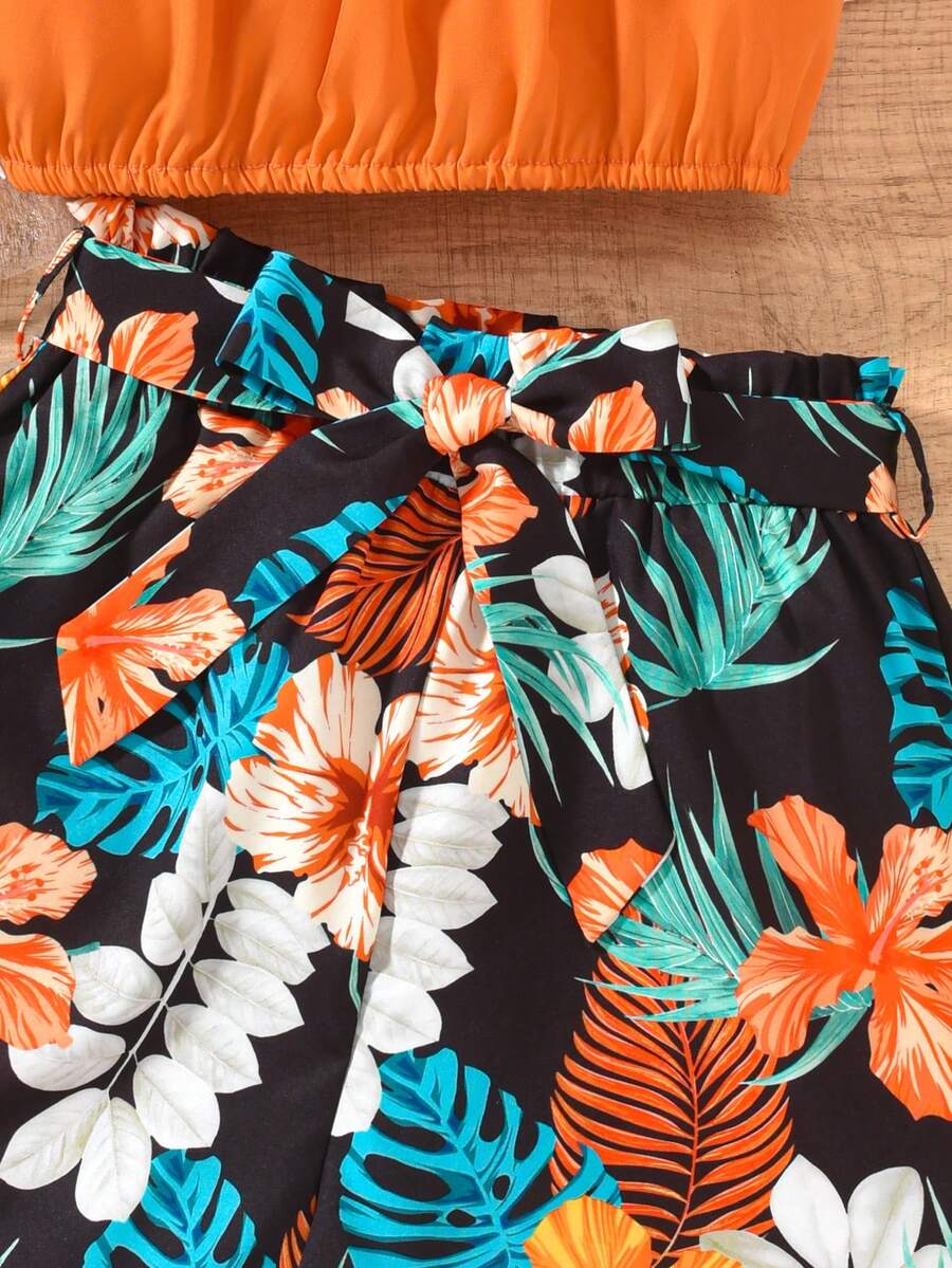 Tween girls 2-piece summer set featuring a black off-shoulder crop top with spaghetti straps and tropical leaf print ruffled paperbag waist shorts with a matching belt.