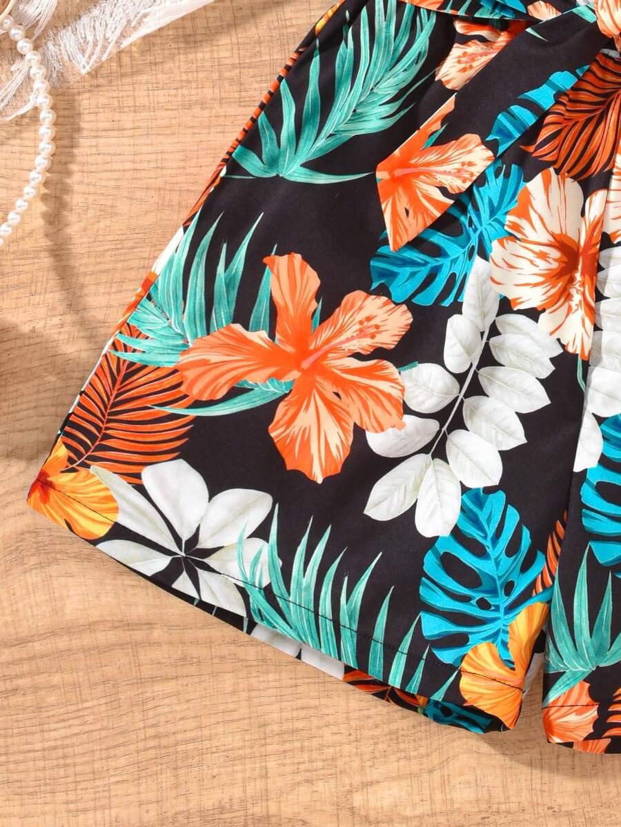 Tween girls 2-piece summer set featuring a black off-shoulder crop top with spaghetti straps and tropical leaf print ruffled paperbag waist shorts with a matching belt.