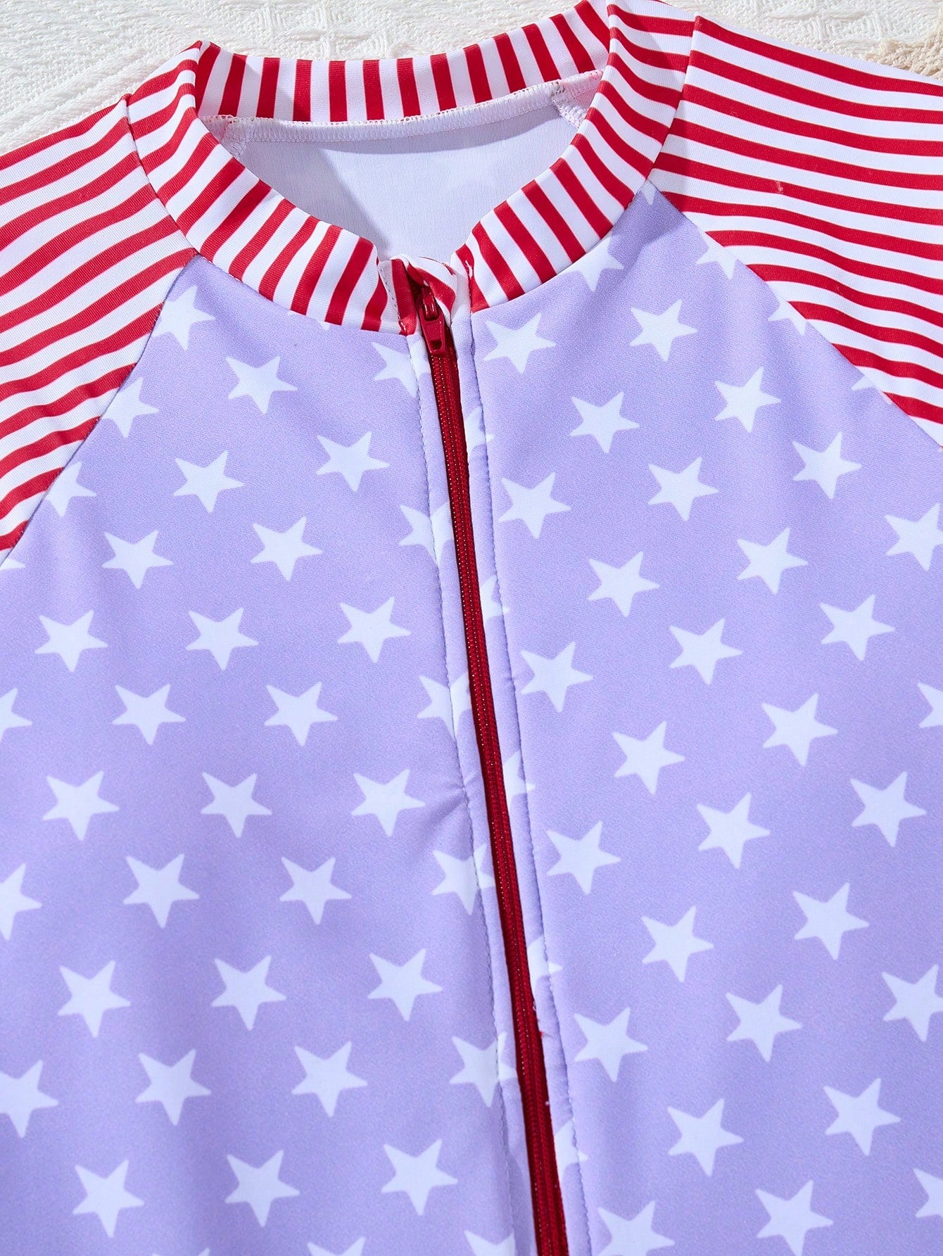Multicolor tween girls one-piece swimsuit with striped and star patchwork design, high neck, ruffle details, zipper and button accents.