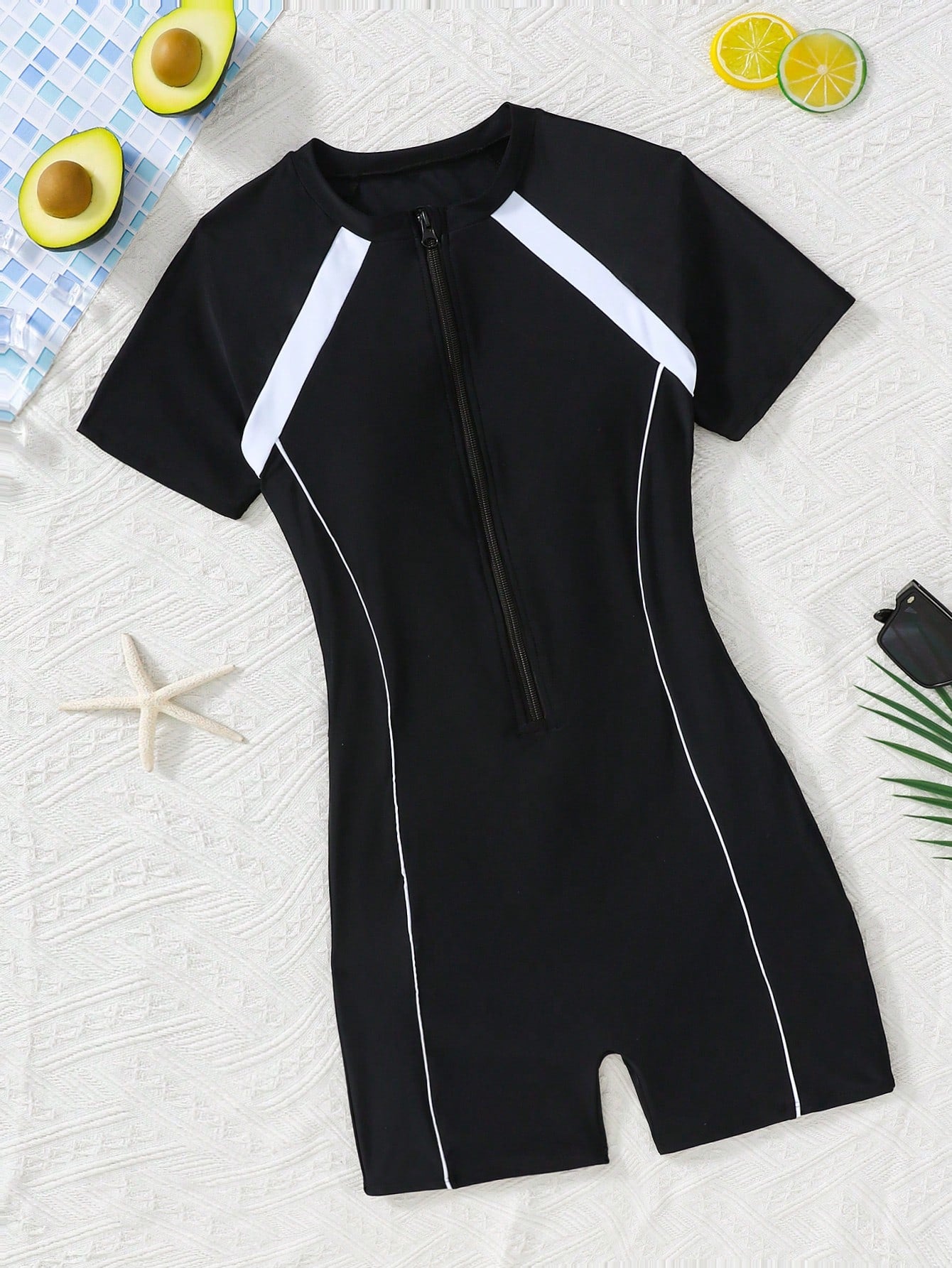 Black and white one-piece rashguard swimsuit for tween girls with short sleeves, high neck, zipper detail, fitted shape, and shorts-style bottom.