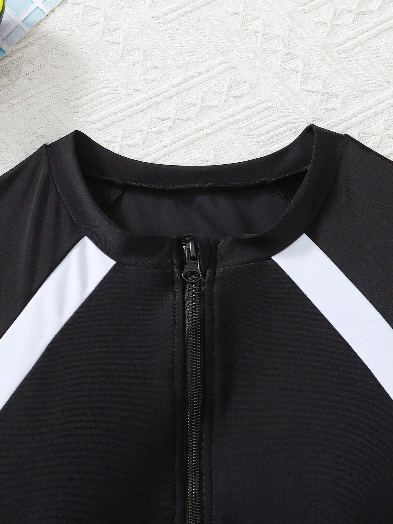 Black and white one-piece rashguard swimsuit for tween girls with short sleeves, high neck, zipper detail, fitted shape, and shorts-style bottom.