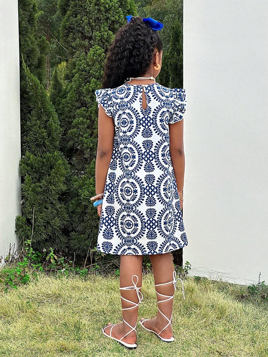 Tween girl wearing a blue ditsy floral patchwork tunic dress with ruffle button details and a round neckline.