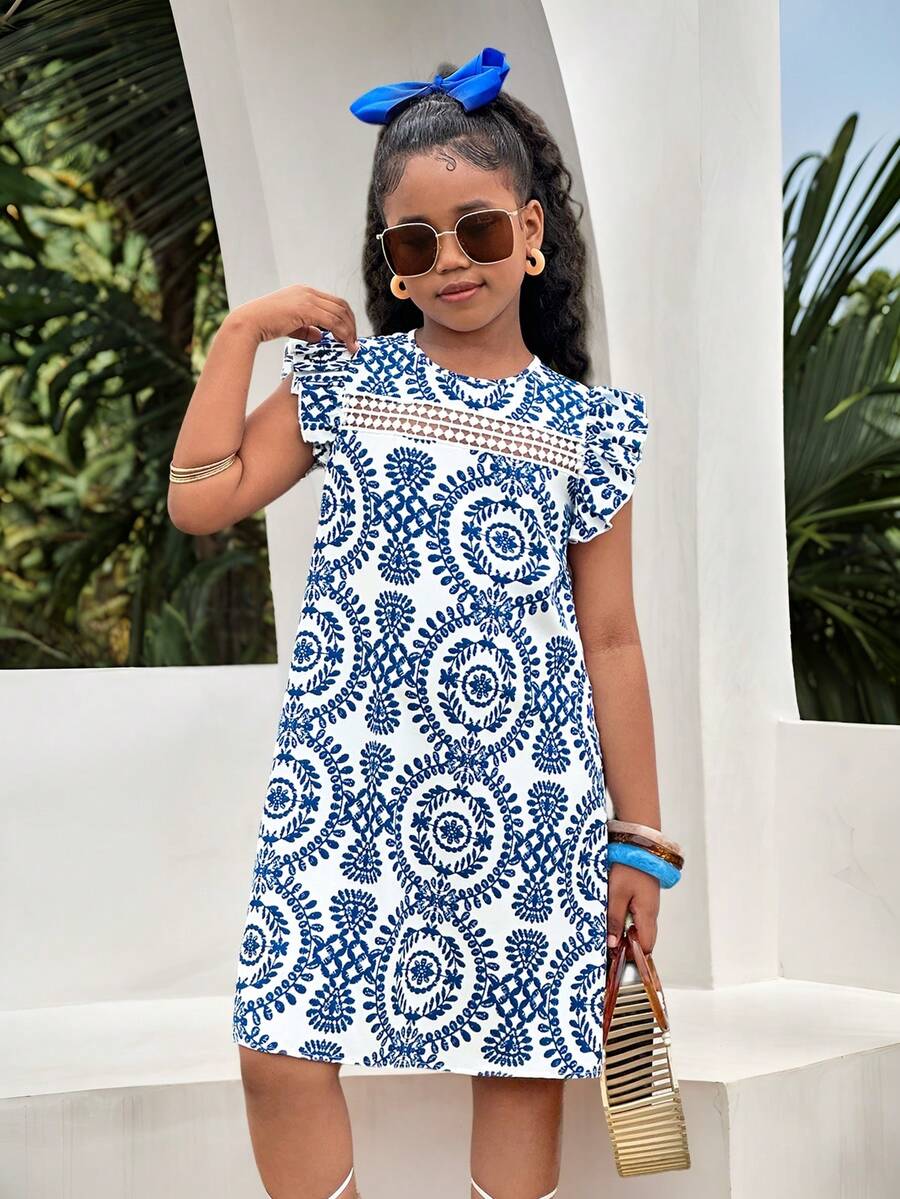 Tween girl wearing a blue ditsy floral patchwork tunic dress with ruffle button details and a round neckline.