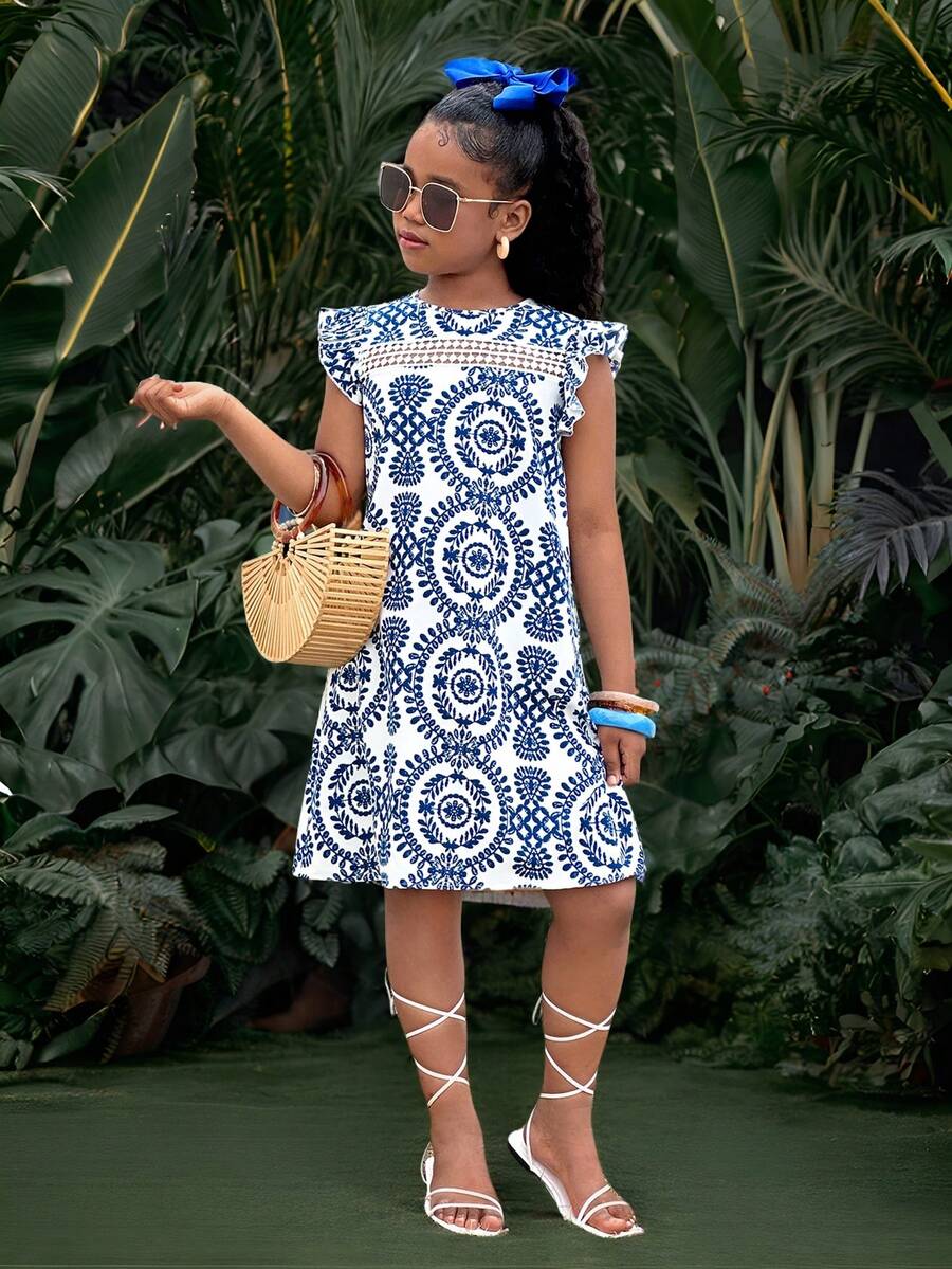 Tween girl wearing a blue ditsy floral patchwork tunic dress with ruffle button details and a round neckline.