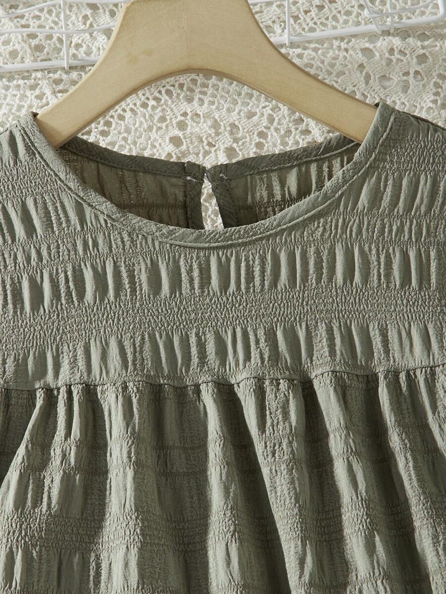 Tween girl wearing an Army Green textured short sleeve smock midi dress with round neck and ruffle flounce hem.
