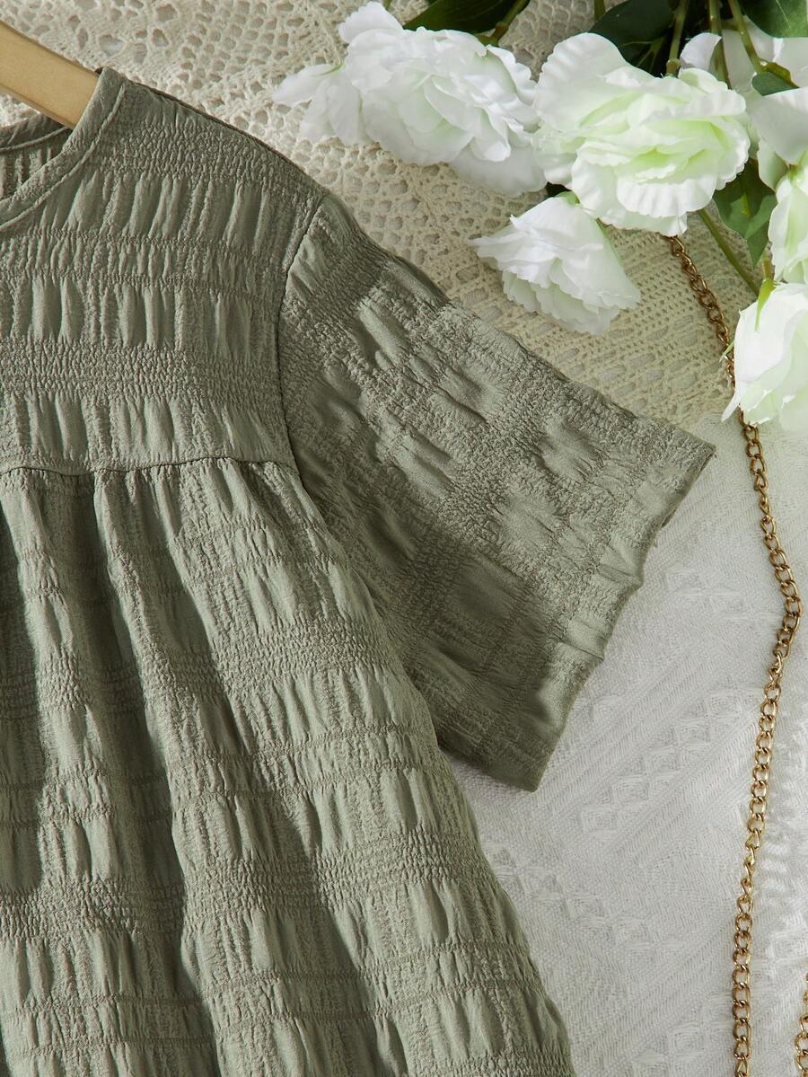 Tween girl wearing an Army Green textured short sleeve smock midi dress with round neck and ruffle flounce hem.