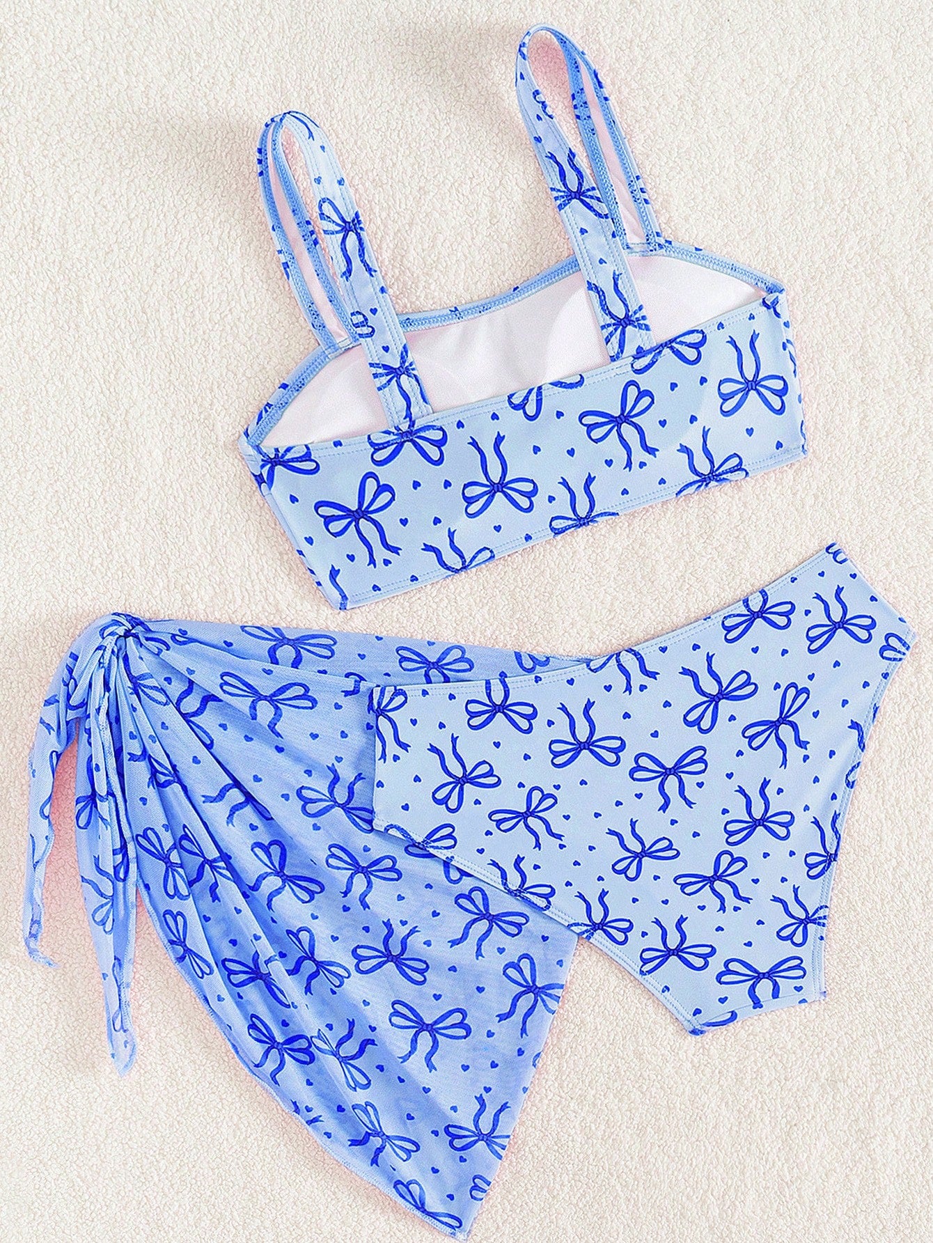 Tween girls three-piece bikini set featuring a bow print bandeau-style top, matching mid-waist bikini bottom, and a sheer mesh cover skirt in a cute beachwear style.