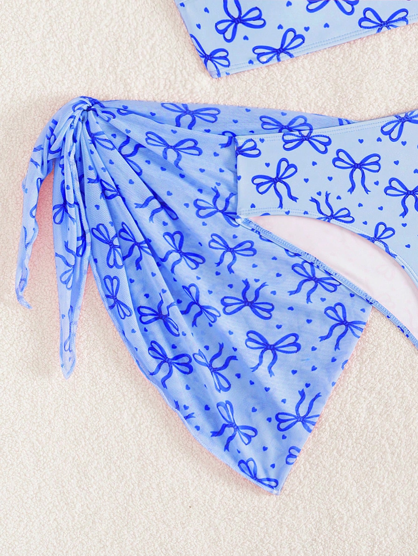Tween girls three-piece bikini set featuring a bow print bandeau-style top, matching mid-waist bikini bottom, and a sheer mesh cover skirt in a cute beachwear style.
