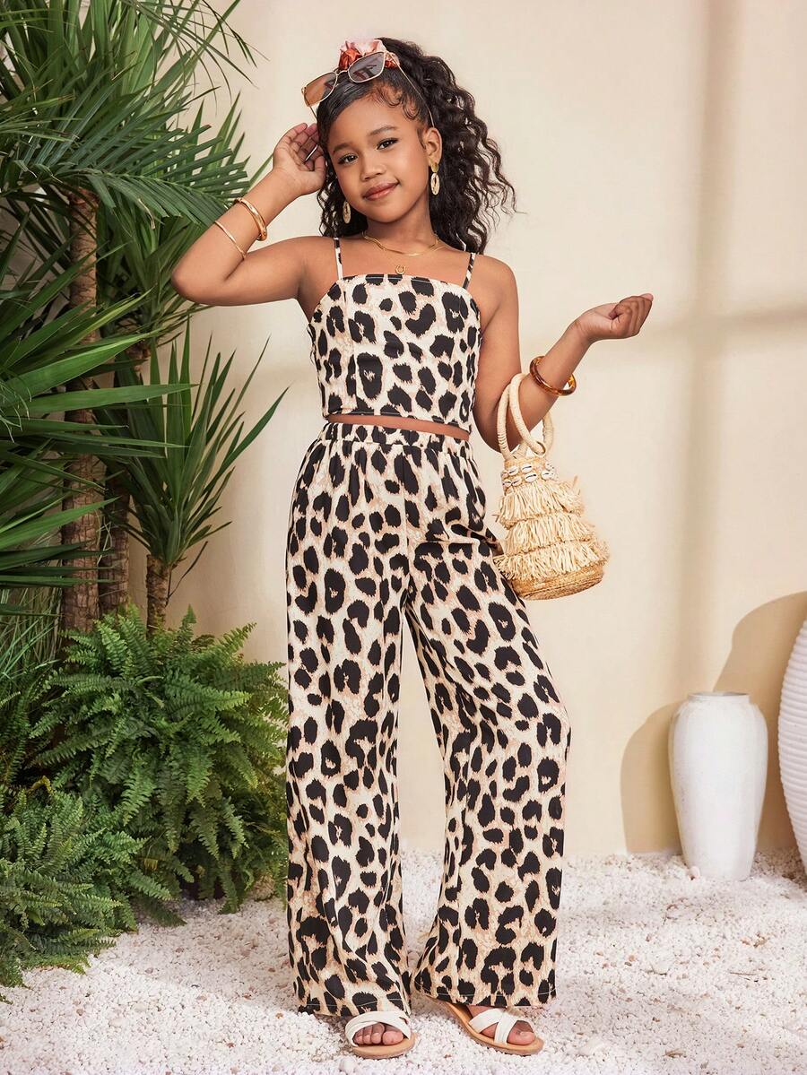 Tween girl wearing a black sleeveless spaghetti strap camisole top with 3D bow decor and matching leopard print wide leg long pants.
