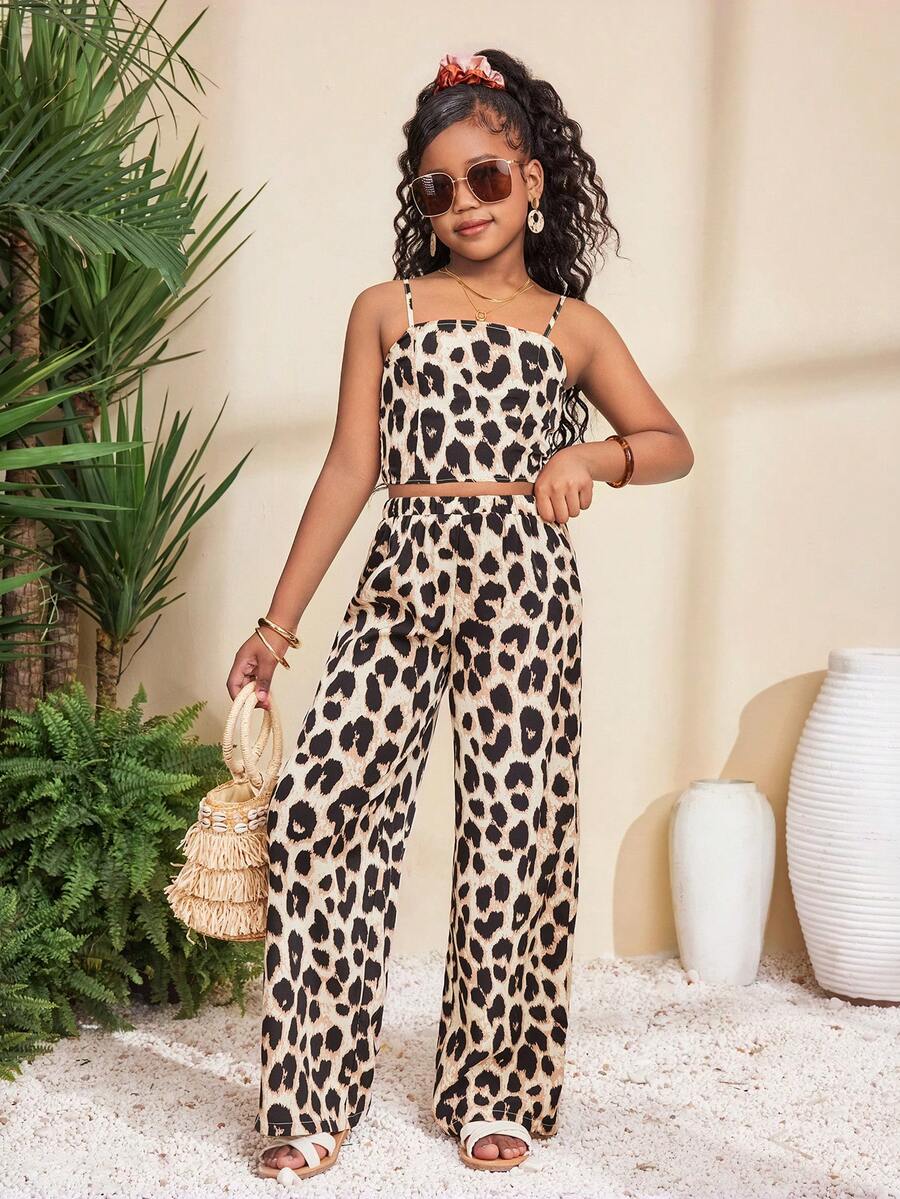 Tween girl wearing a black sleeveless spaghetti strap camisole top with 3D bow decor and matching leopard print wide leg long pants.