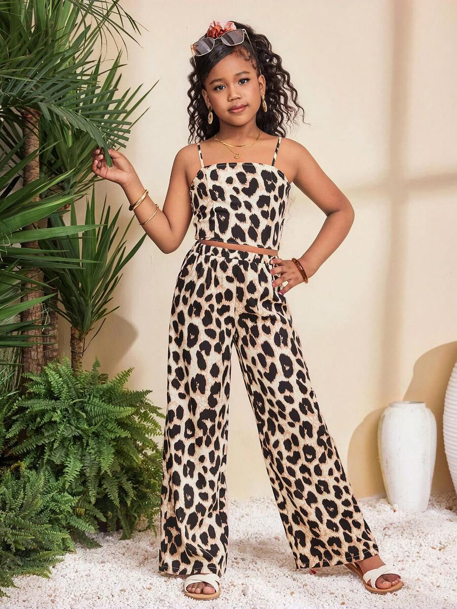 Tween girl wearing a black sleeveless spaghetti strap camisole top with 3D bow decor and matching leopard print wide leg long pants.