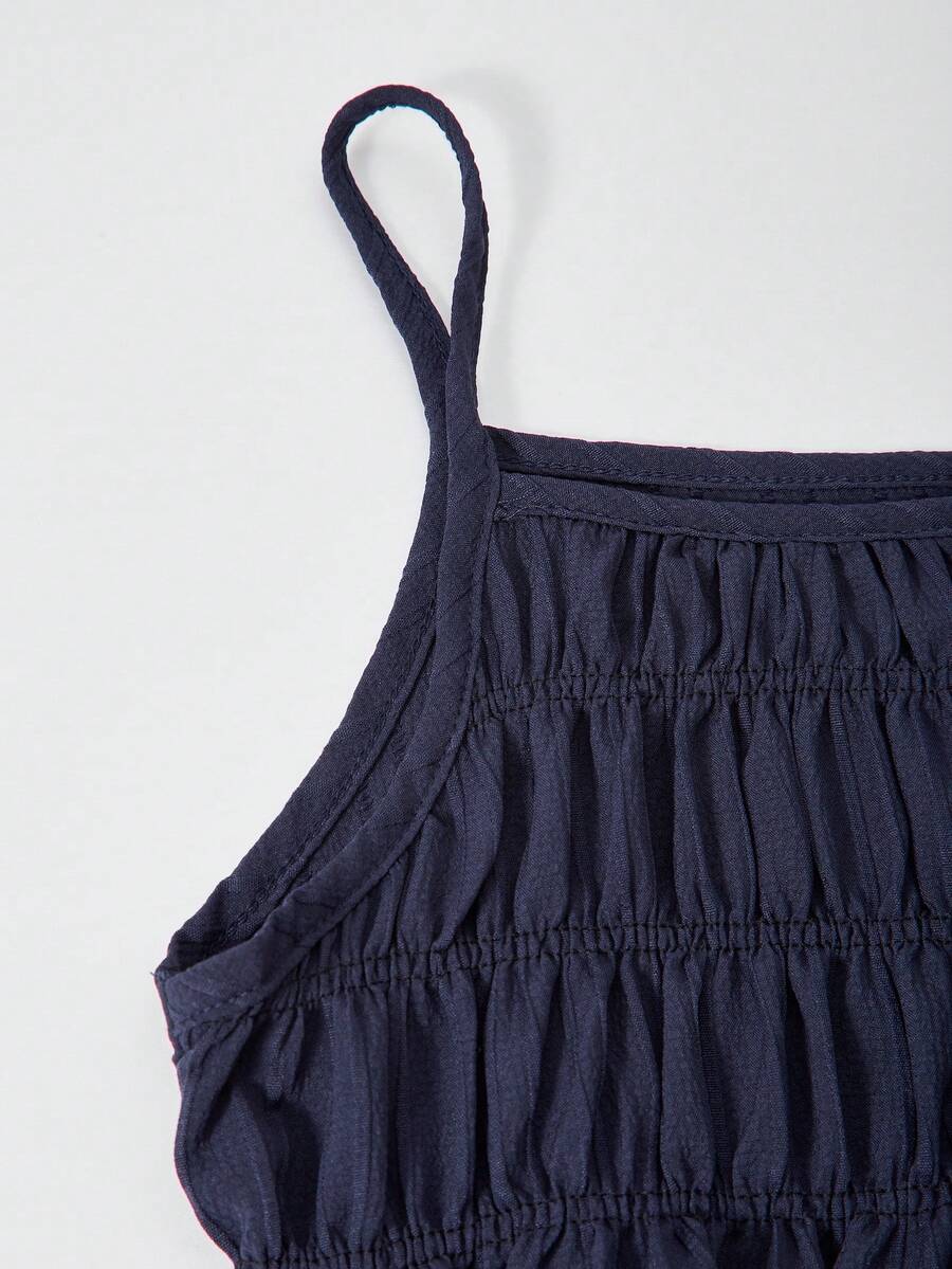 Tween girl wearing an apricot 2-piece outfit set featuring a shirred spaghetti strap short cami top and matching wide-leg long pants.