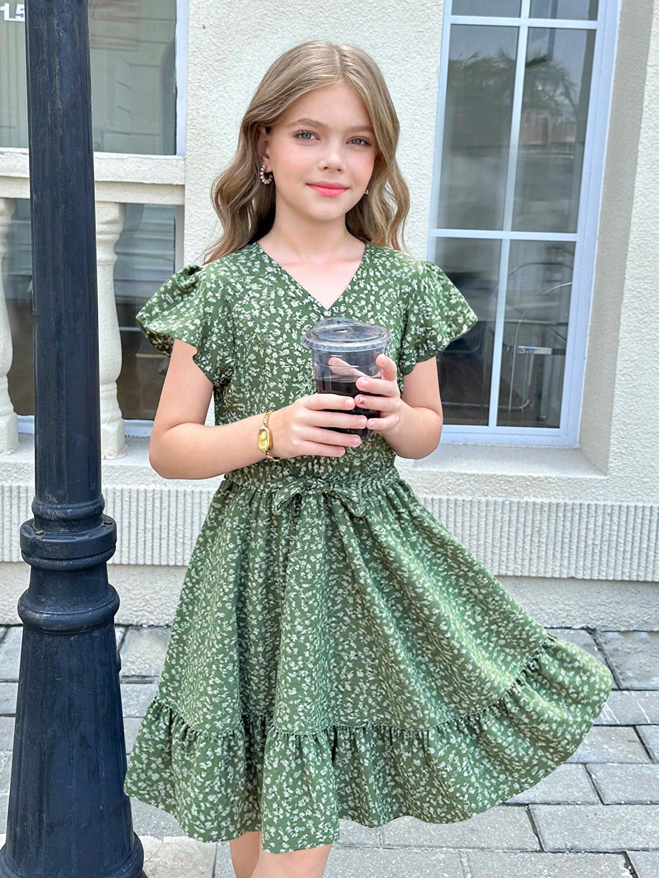 Tween girl wearing a black ditsy floral A-line short dress with V-neckline and flounce short sleeves.