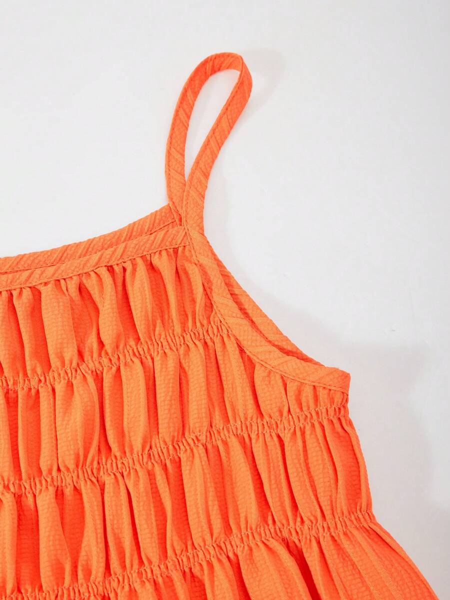 Tween girl wearing an apricot 2-piece outfit set featuring a shirred spaghetti strap short cami top and matching wide-leg long pants.