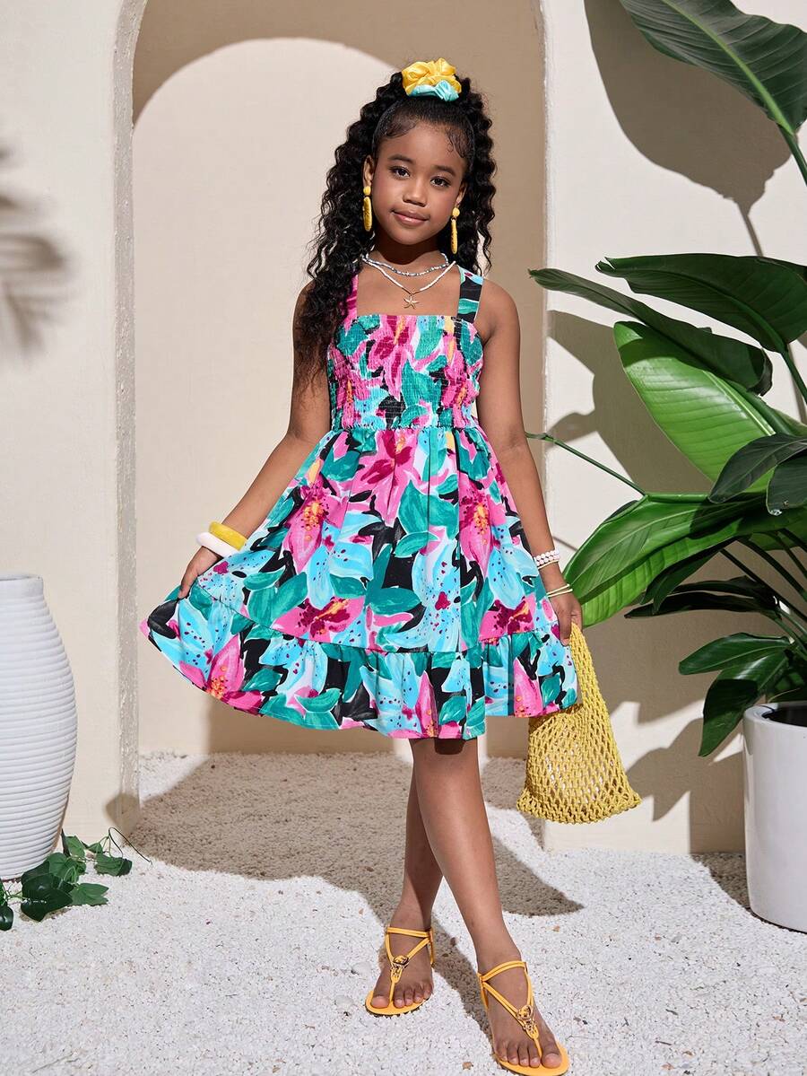 Pink sleeveless tween girls vacation dress with all-over fruit and vegetable print, strap neckline, belted high waist, cut-out detail, and flared ruffle hem.