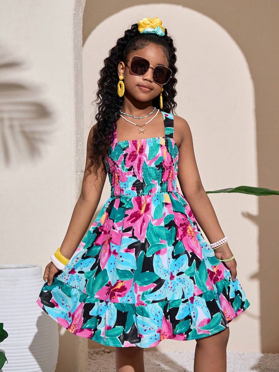Pink sleeveless tween girls vacation dress with all-over fruit and vegetable print, strap neckline, belted high waist, cut-out detail, and flared ruffle hem.