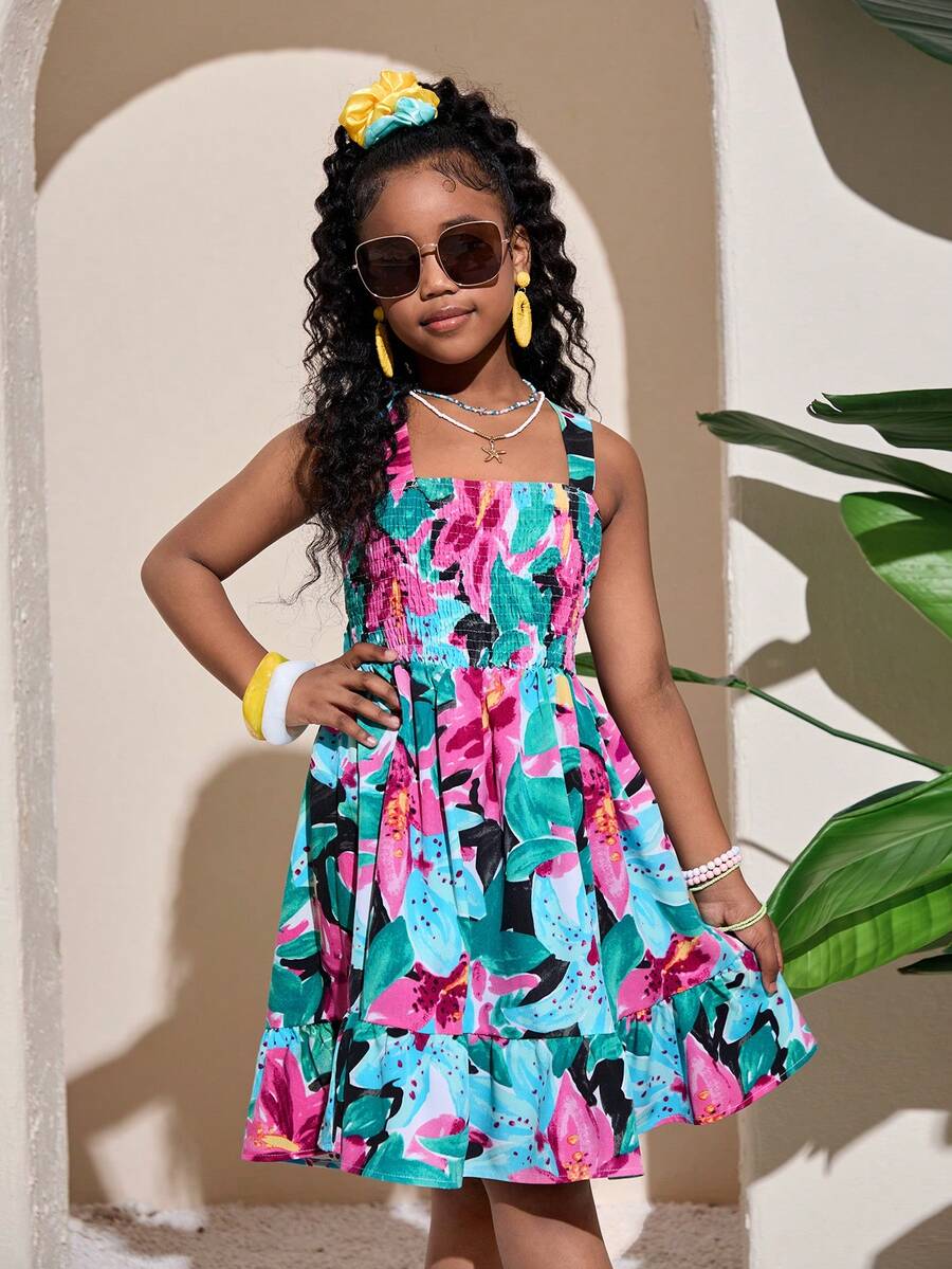 Pink sleeveless tween girls vacation dress with all-over fruit and vegetable print, strap neckline, belted high waist, cut-out detail, and flared ruffle hem.