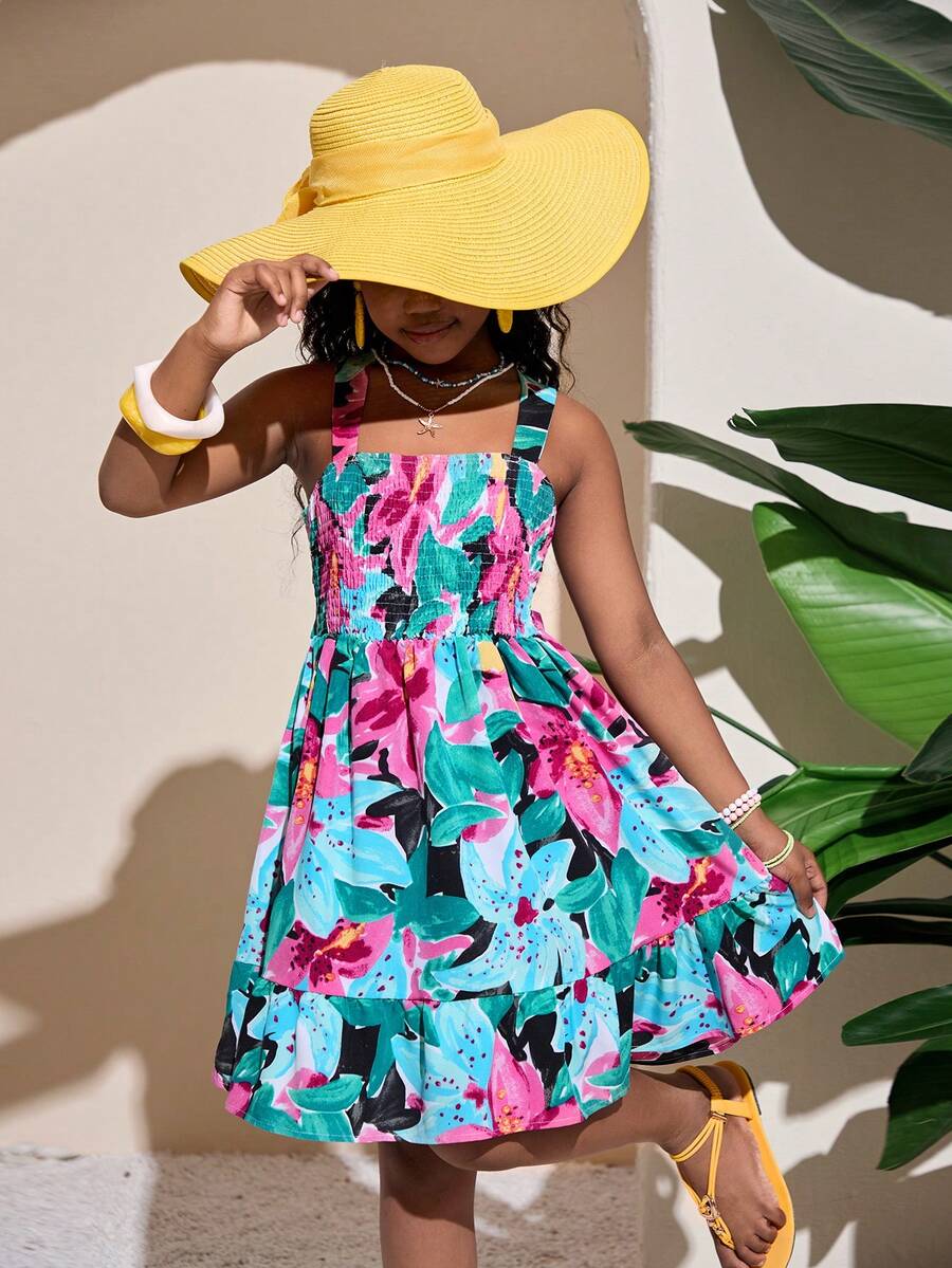 Pink sleeveless tween girls vacation dress with all-over fruit and vegetable print, strap neckline, belted high waist, cut-out detail, and flared ruffle hem.
