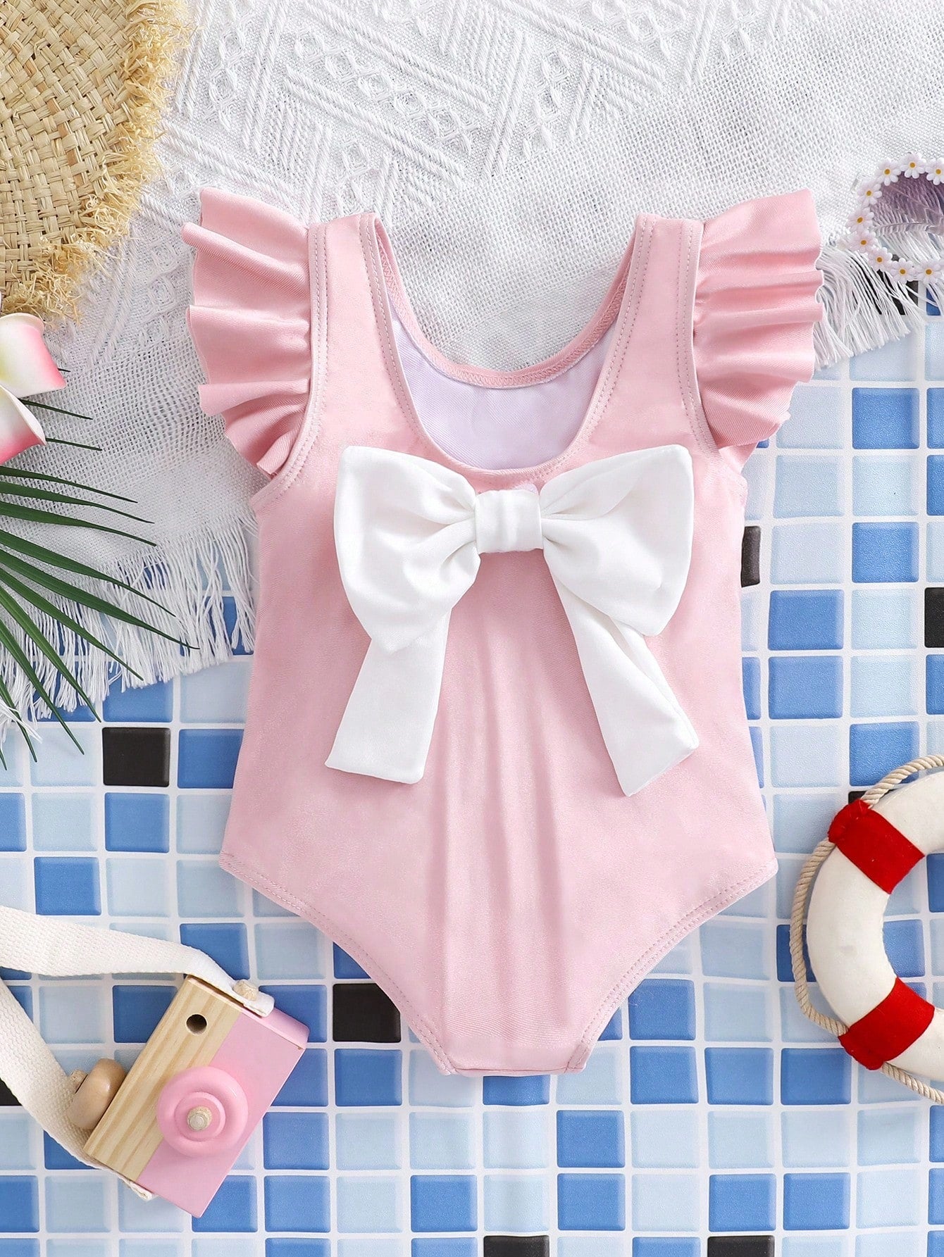 Baby pink colorblock one-piece swimsuit for tween girls with ruffle details, bow decor, scoop neckline, and fitted vacation swimwear style.