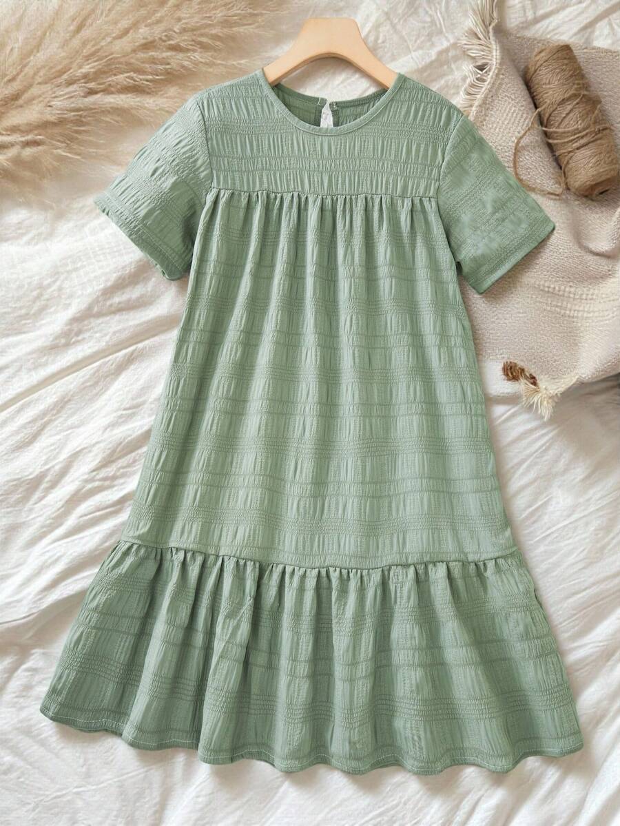 Tween girl wearing an Army Green textured short sleeve smock midi dress with round neck and ruffle flounce hem.