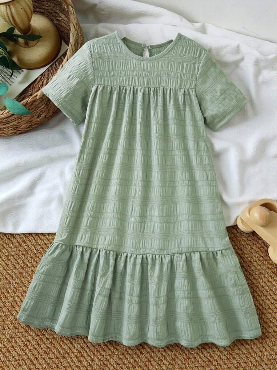 Tween girl wearing an Army Green textured short sleeve smock midi dress with round neck and ruffle flounce hem.