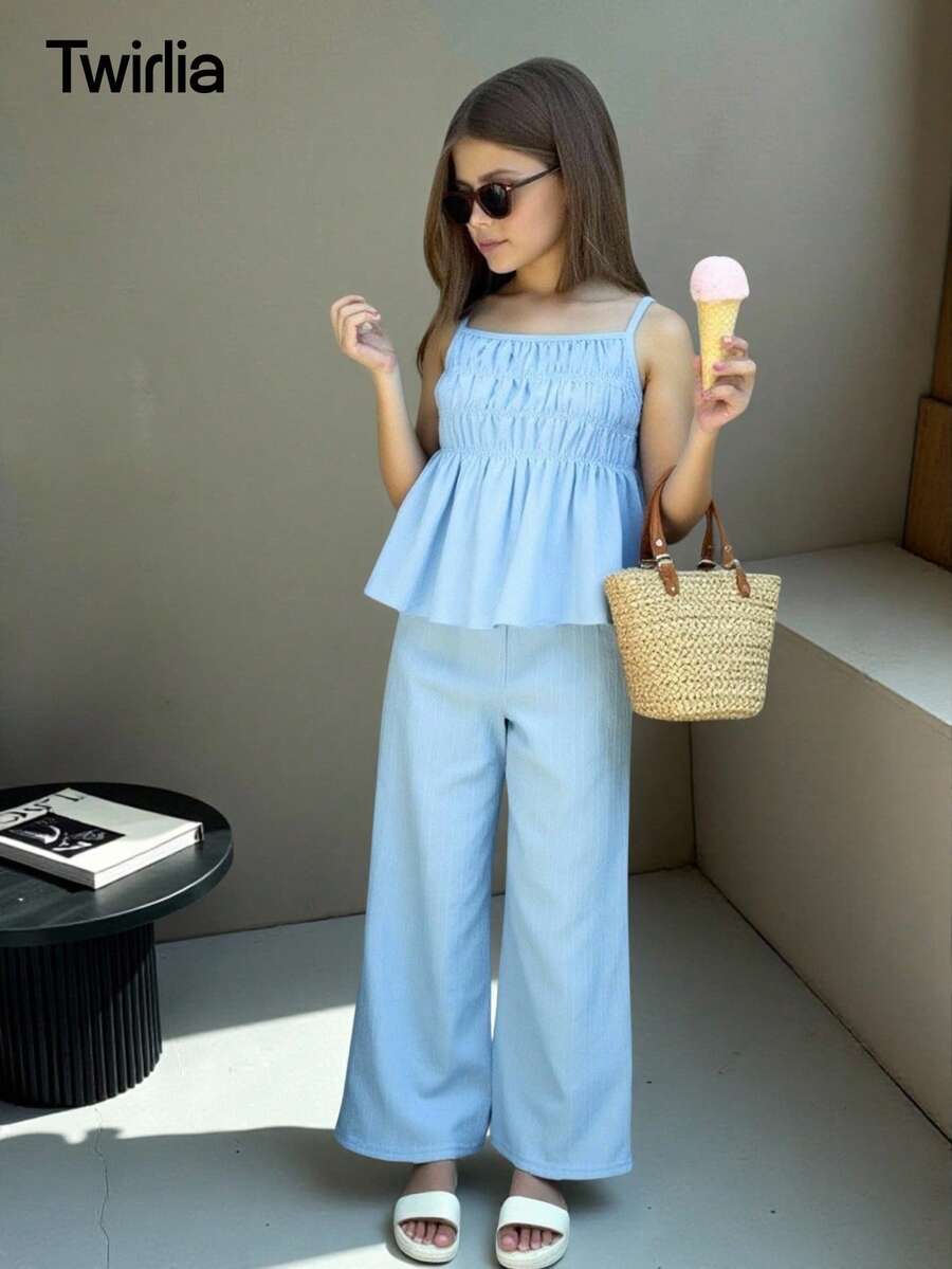 Tween girl wearing an apricot 2-piece outfit set featuring a shirred spaghetti strap short cami top and matching wide-leg long pants.