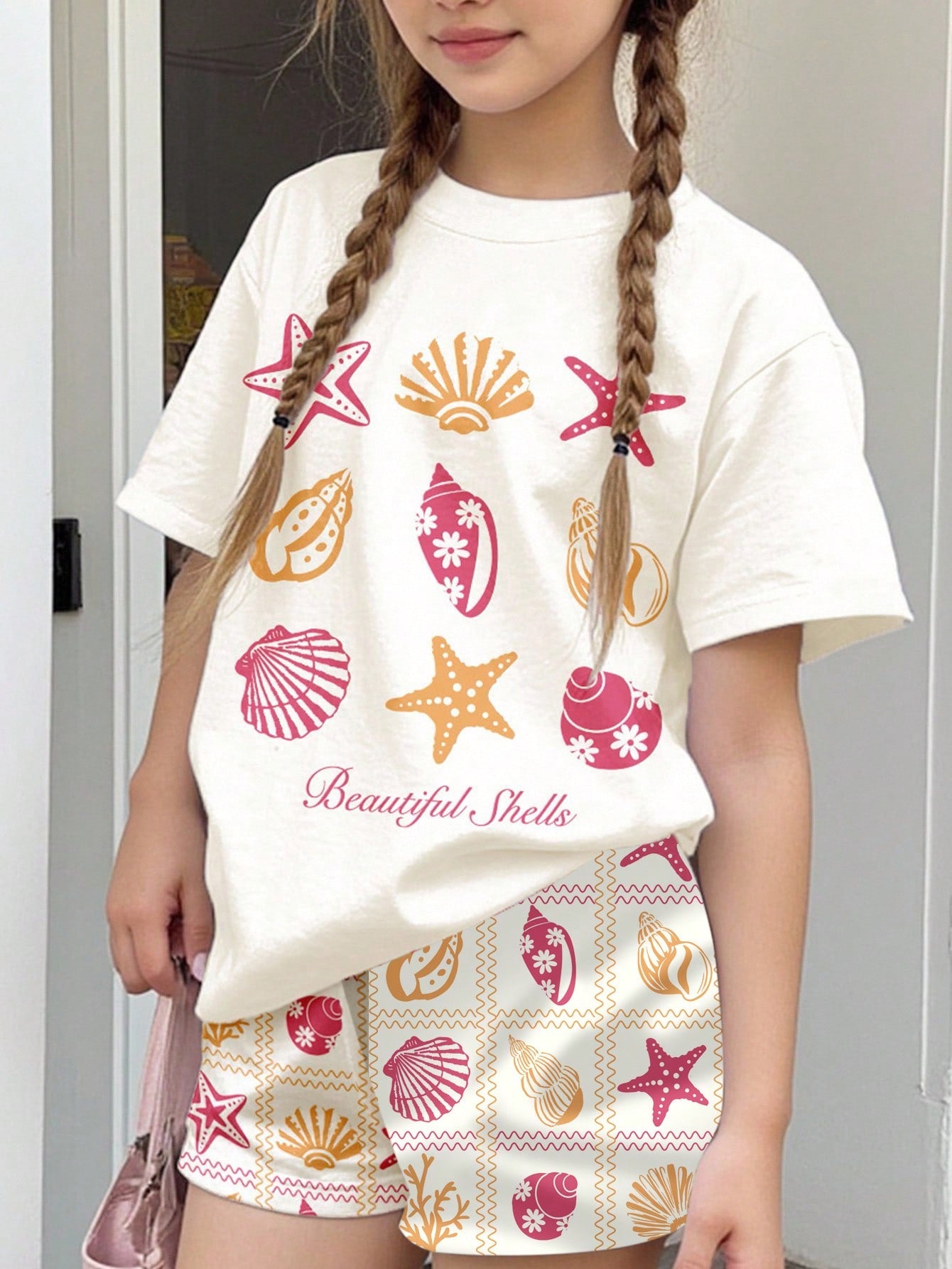 Tween girls 2-piece summer casual outfit featuring a multicolor seashell print short sleeve T-shirt with drop shoulders and matching loose fit shorts with pockets.