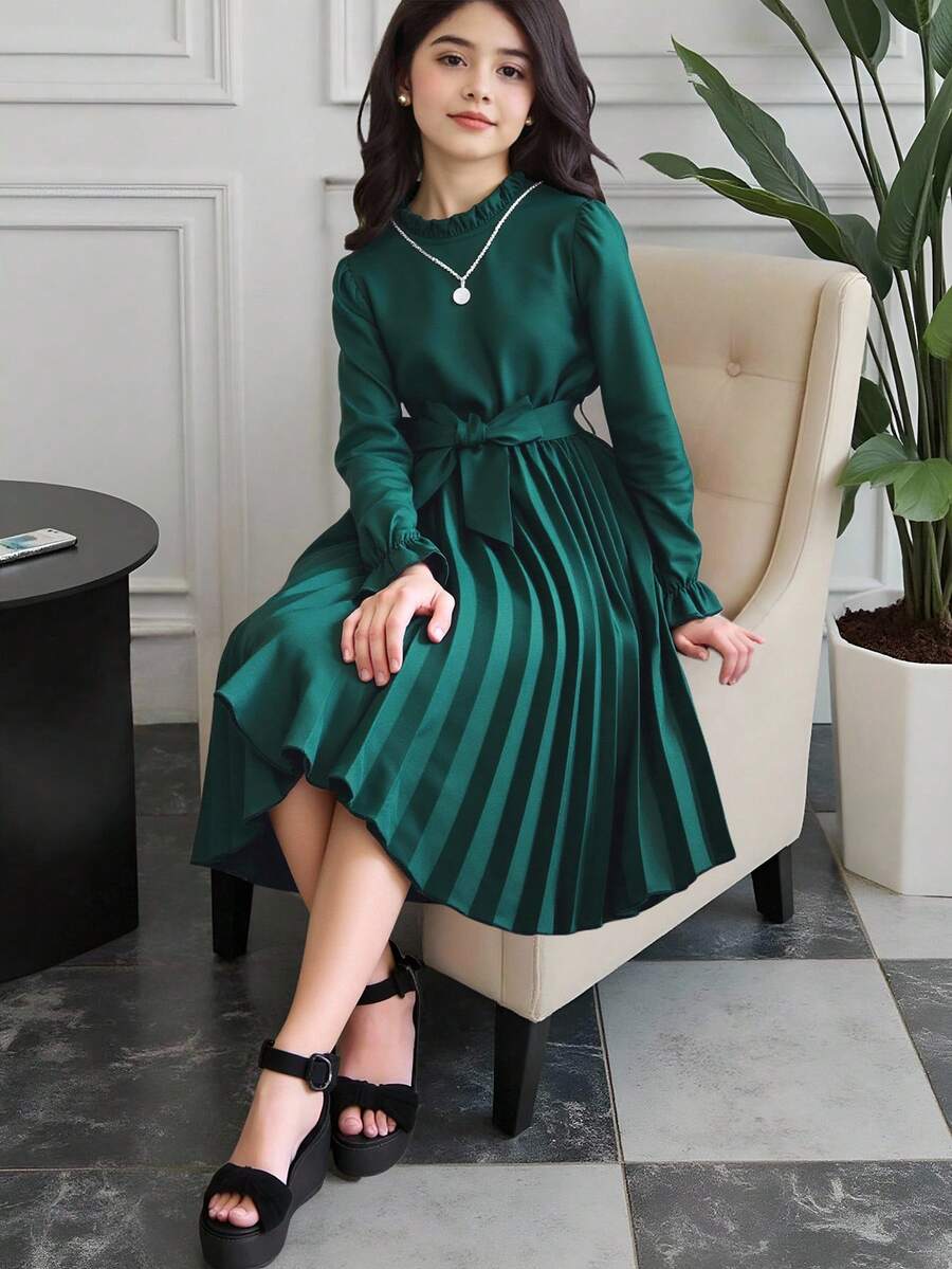 Tween girl wearing a royal blue long sleeve pleated casual A-line dress featuring a stand collar, flare sleeves, high waist with front tie belt, and ruffle hem.