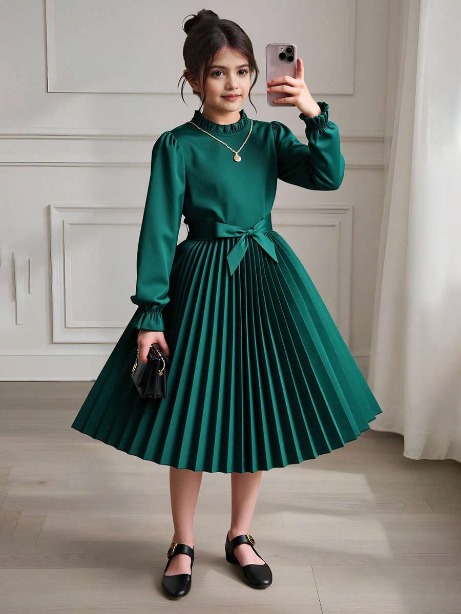 Tween girl wearing a royal blue long sleeve pleated casual A-line dress featuring a stand collar, flare sleeves, high waist with front tie belt, and ruffle hem.