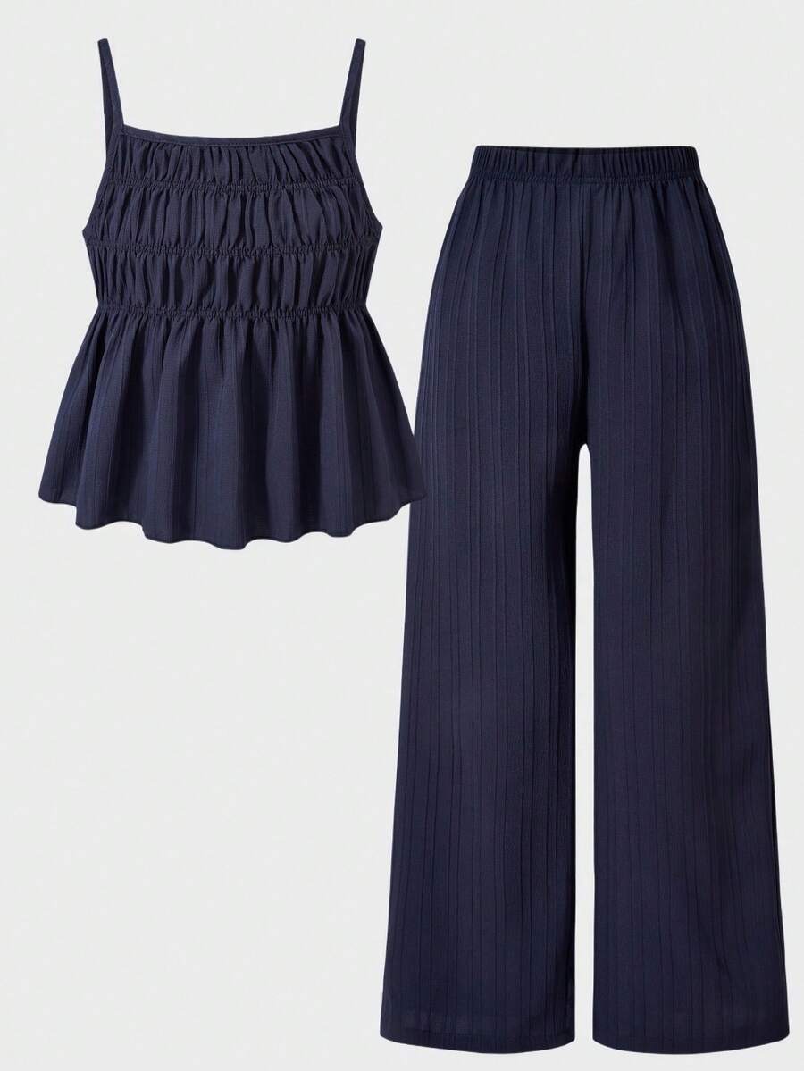 Tween girl wearing an apricot 2-piece outfit set featuring a shirred spaghetti strap short cami top and matching wide-leg long pants.