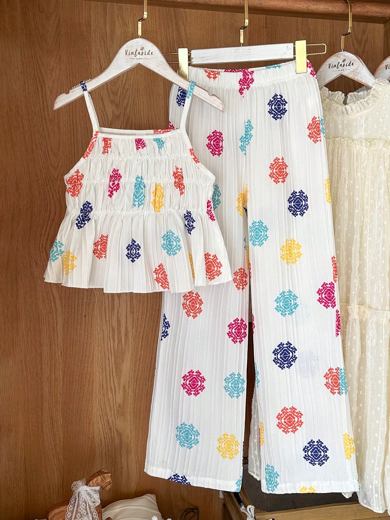 Tween girl wearing an apricot 2-piece outfit set featuring a shirred spaghetti strap short cami top and matching wide-leg long pants.