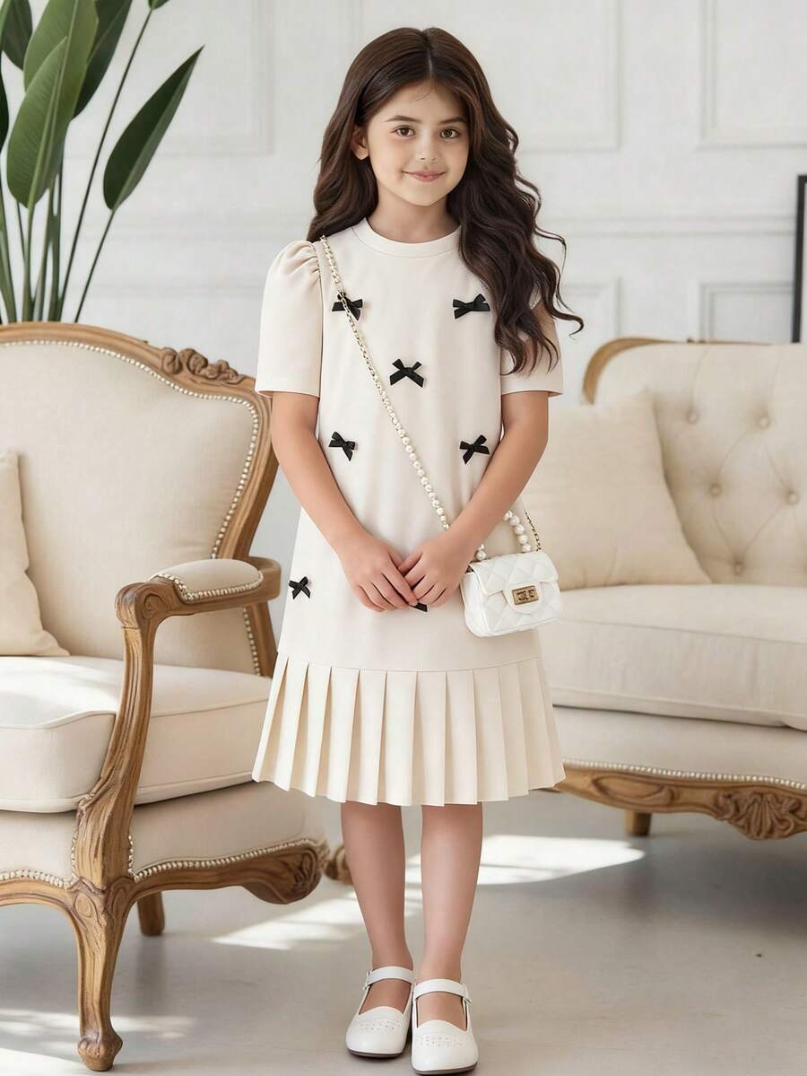 Tween girls apricot short-sleeve pleated smock dress with 3D bow decor and round neckline.
