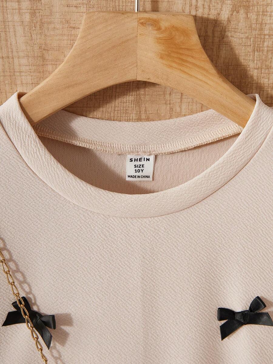 Tween girls apricot short-sleeve pleated smock dress with 3D bow decor and round neckline.