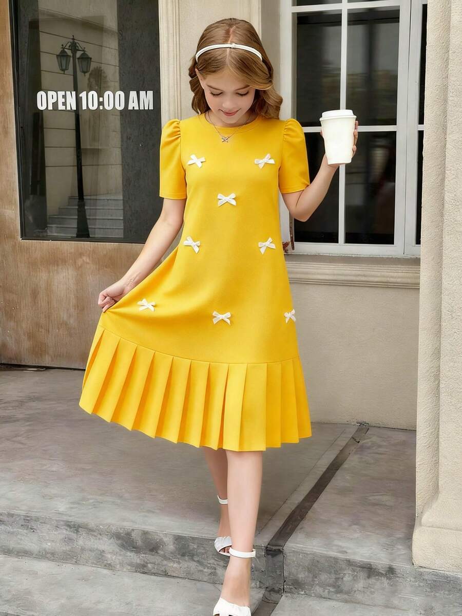 Tween girls apricot short-sleeve pleated smock dress with 3D bow decor and round neckline.