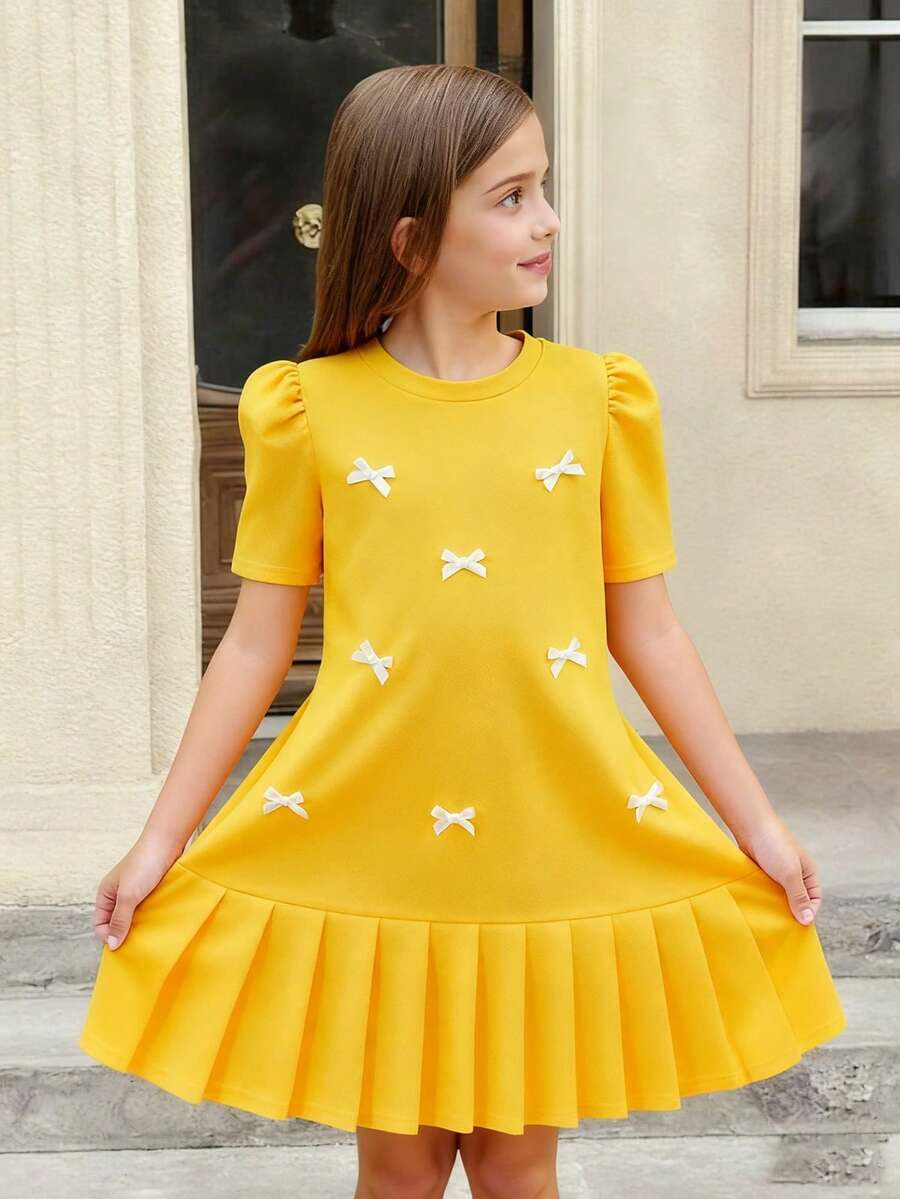Tween girls apricot short-sleeve pleated smock dress with 3D bow decor and round neckline.