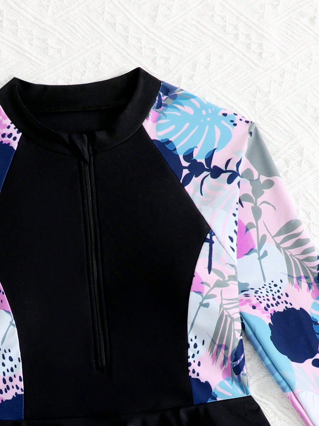 Tween girls one-piece swimsuit in black floral pattern with long sleeves, high neck, front zipper, and a skirt-style bottom.