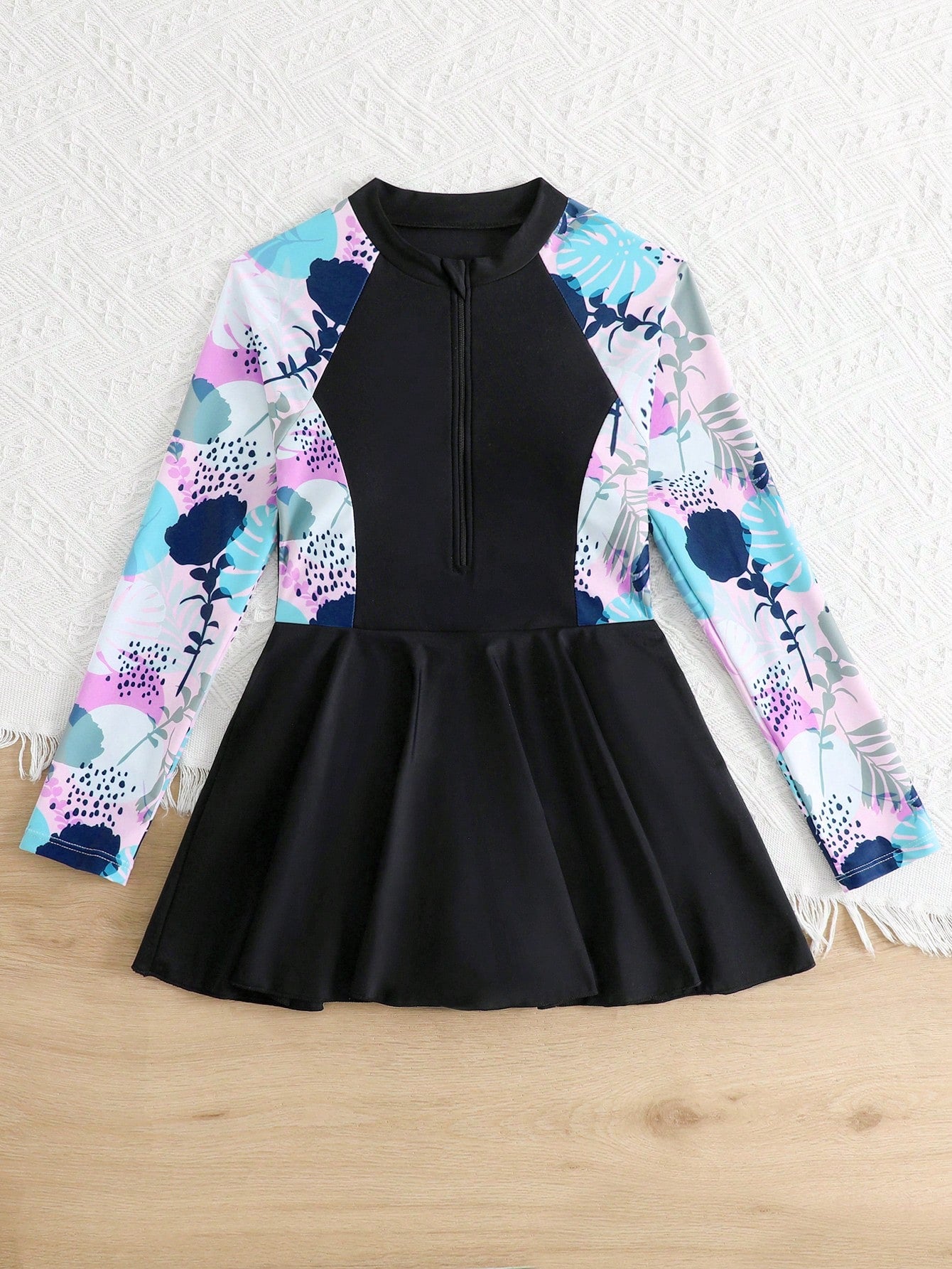 Tween girls one-piece swimsuit in black floral pattern with long sleeves, high neck, front zipper, and a skirt-style bottom.