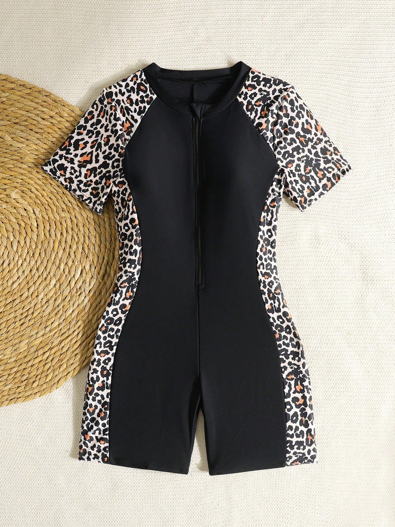 Black and white one-piece rashguard swimsuit for tween girls with short sleeves, high neck, zipper detail, fitted shape, and shorts-style bottom.