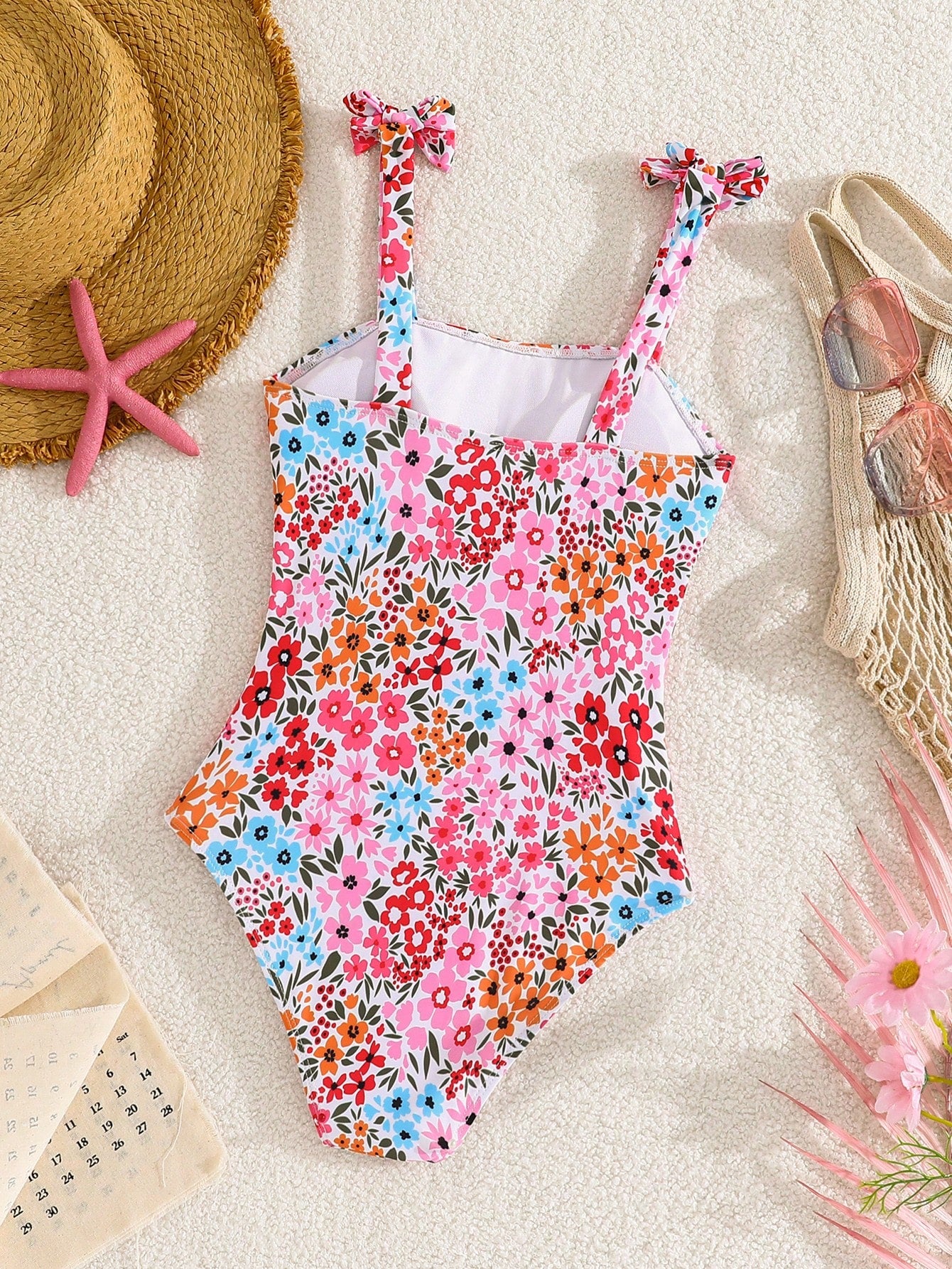 Tween girl floral print one-piece swimsuit with twist front, spaghetti straps, fitted shape, and multicolor all-over hibiscus-inspired pattern for beach and pool wear.